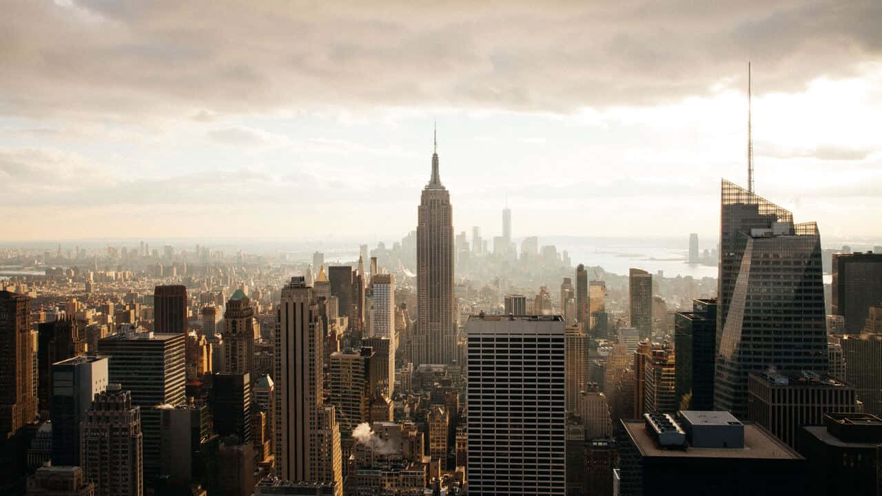 720p Empire State Building 桌布 壁紙 — 紐約市天際線的日出全景，帝國大廈在柔和的金色天空下聳立於摩天大樓的海洋之上。