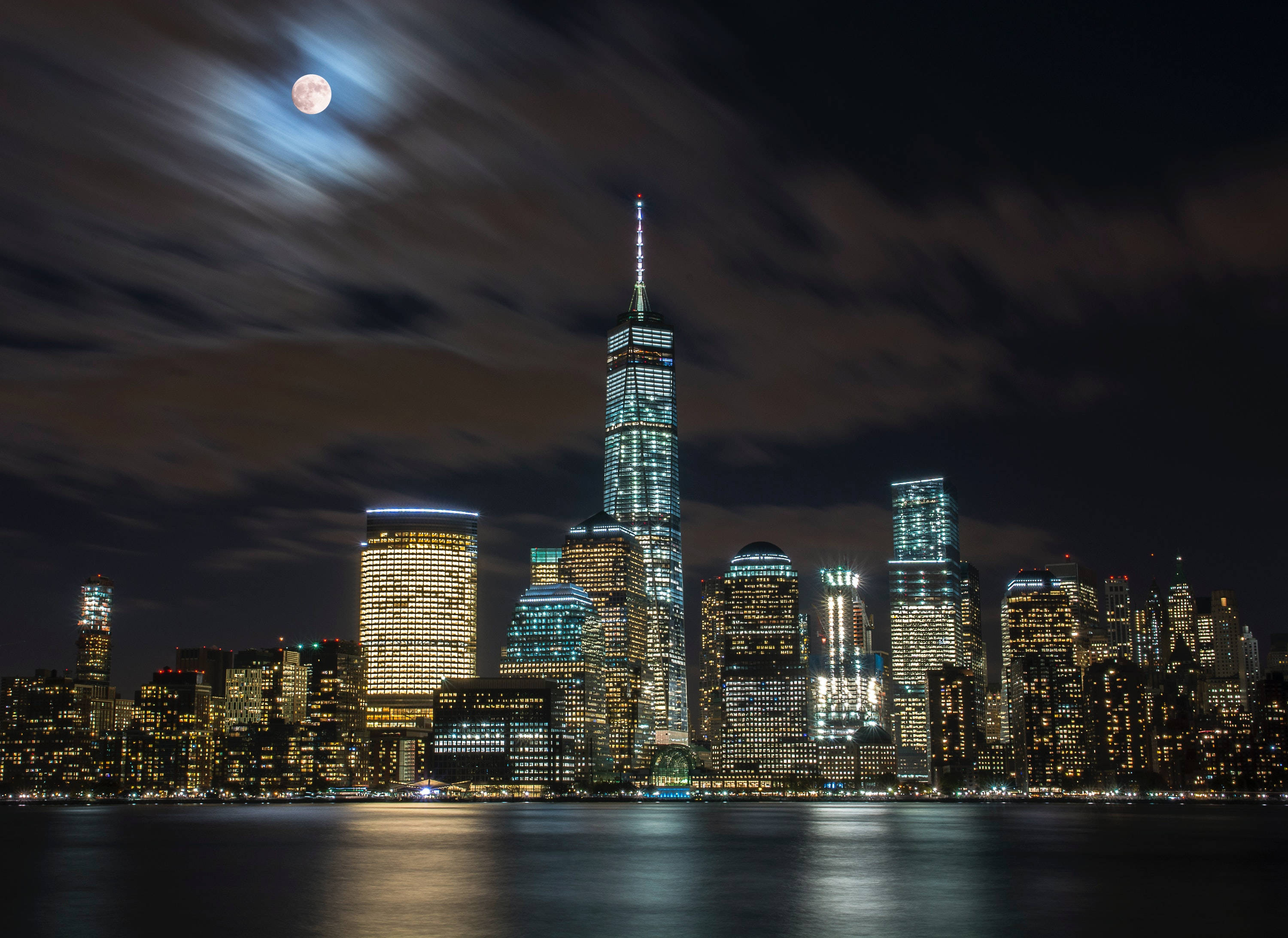 Nyc Aesthetic 桌布 壁紙 — 紐約市天際線的月光夜景，摩天大樓倒映在水中，雲朵在頭頂飄過。