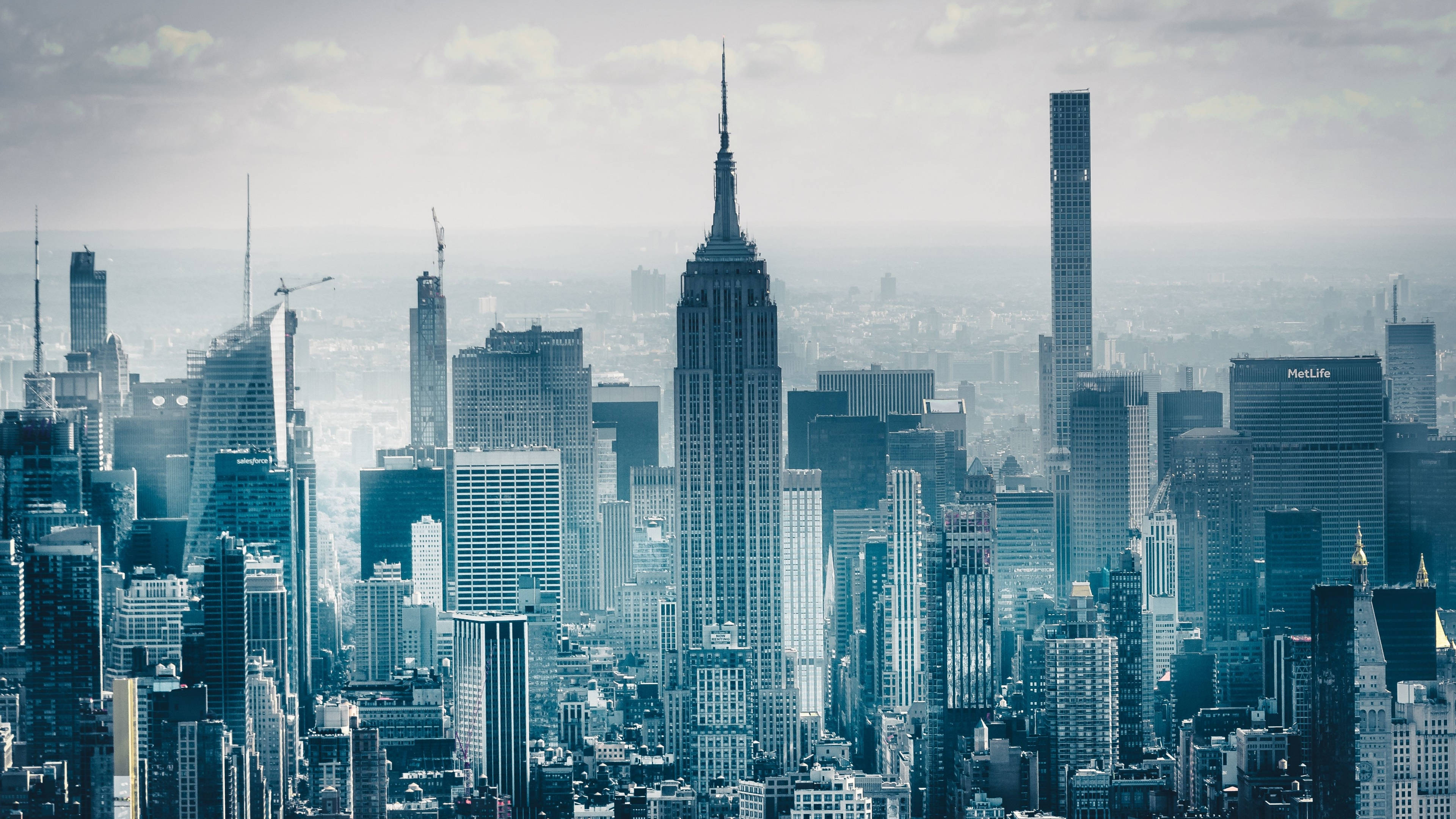New York 桌布 壁紙 — 紐約市天際線的朦朧藍色全景，以帝國大廈和現代摩天大樓為主，天空多雲。