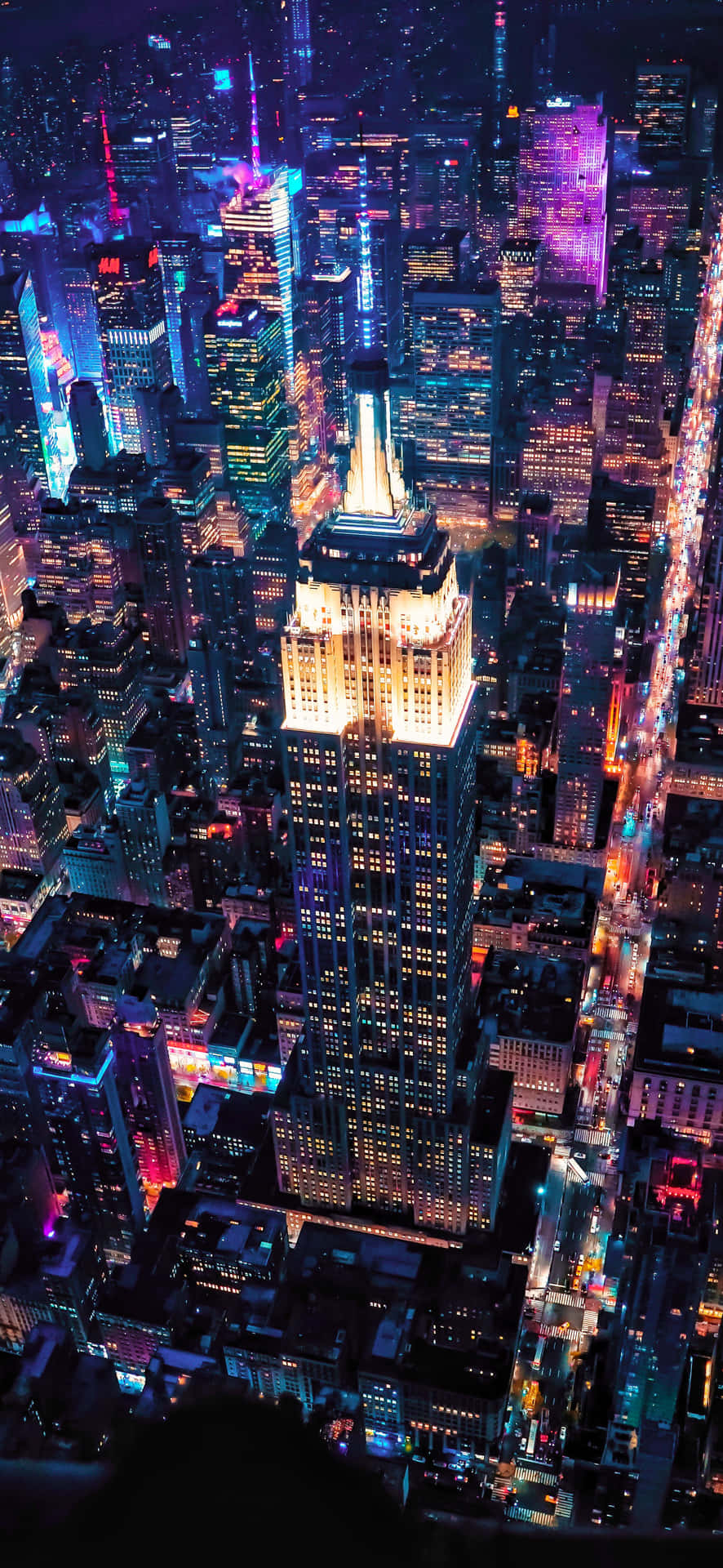 Aerial View Of The Dark City Buildings 4K Phone Wallpaper 壁紙 — 紐約市天際線的空中夜景，帝國大廈在霓虹燈閃爍的摩天大樓中溫暖地發光。