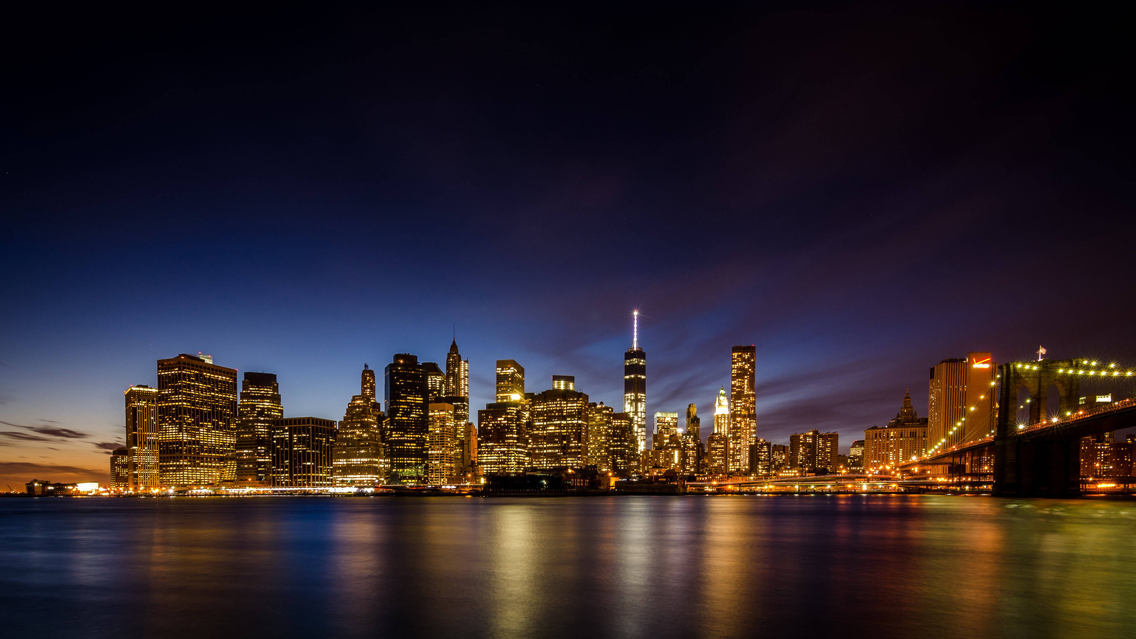 4K New York City 桌布 壁紙 — 紐約市天際線的絕美夜景，摩天大樓燈火通明，布魯克林大橋倒映在平靜的水面上。