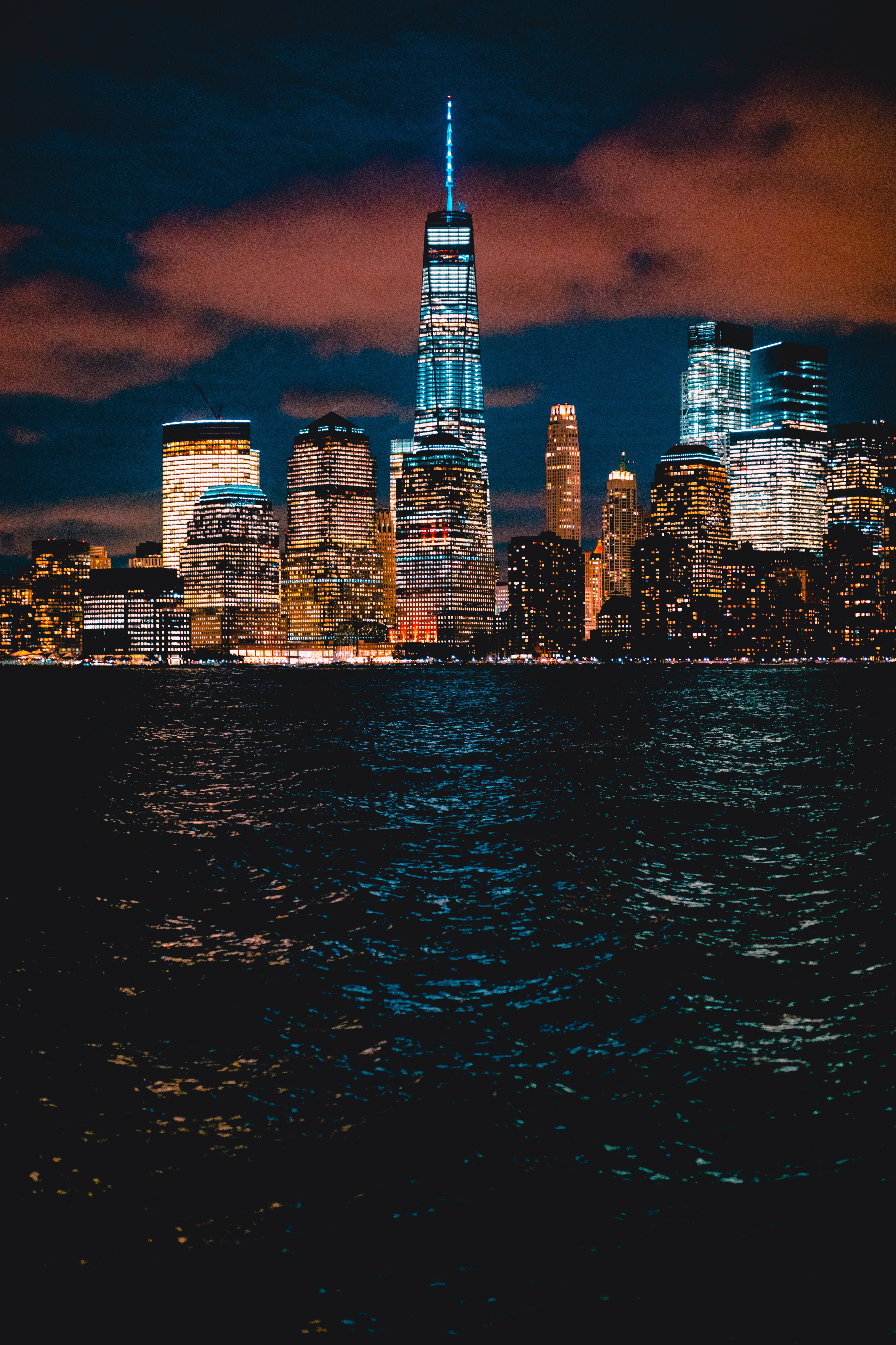 New 桌布 壁紙 — 紐約市天際線的迷人夜景，在陰暗的天空下，明亮的摩天大樓倒映在黑暗的水面上。