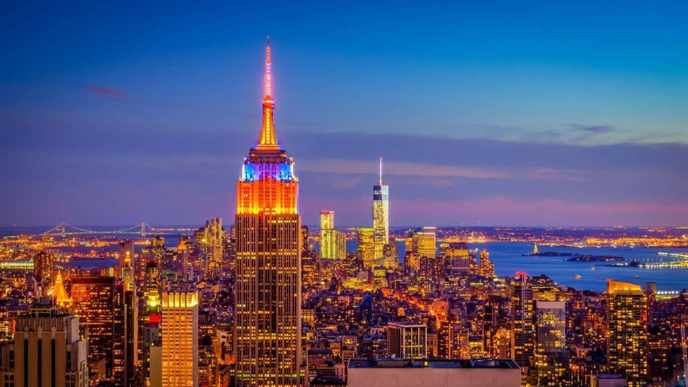 1366x768 Empire State Building 桌布 壁紙 — 紐約市天際線的迷人黃昏景色，帝國大廈在深藍色天空的襯托下閃閃發光。
