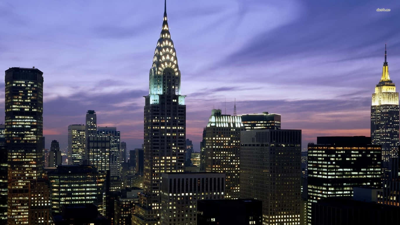 1366x768 Empire State Building 桌布 壁紙 — 紐約市天際線的迷人黃昏景色，摩天大樓在紫色和橙色的天空下亮起燈光。