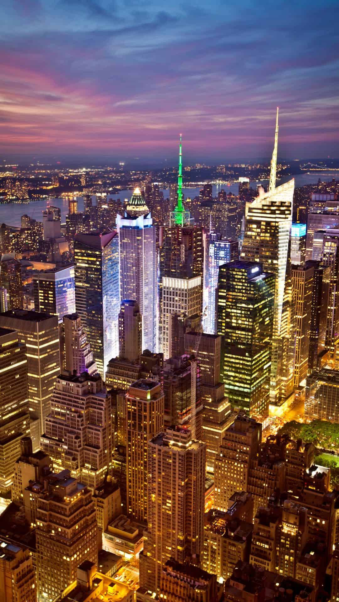 new york city iPhone x 桌布 壁紙 — 紐約市天際線的鳥瞰圖，在黃昏時分，摩天大樓在紫色和粉紅色的天空下閃閃發光。