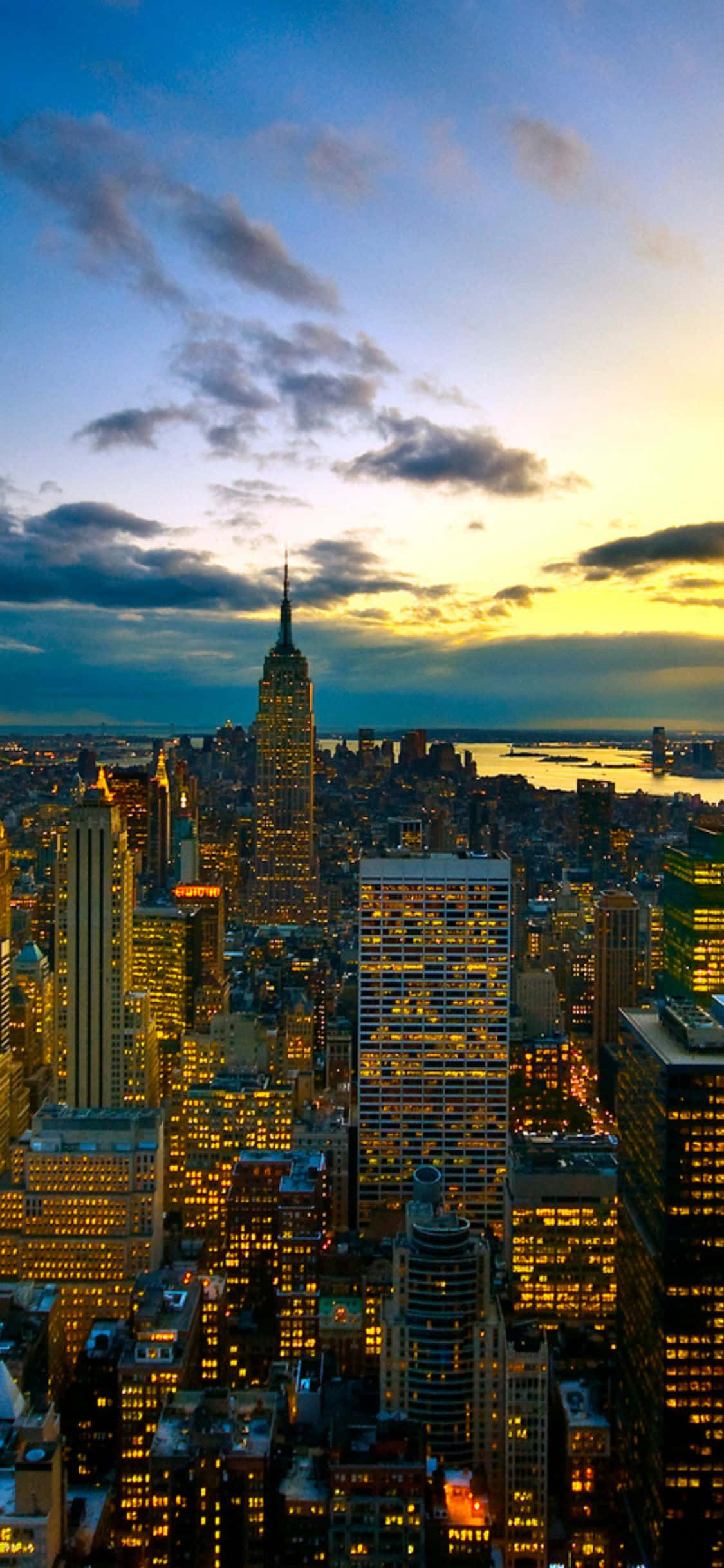 iPhone X New York 桌布 壁紙 — 紐約市天際線的鳥瞰圖，夕陽下金色摩天大樓和戲劇性的雲彩。
