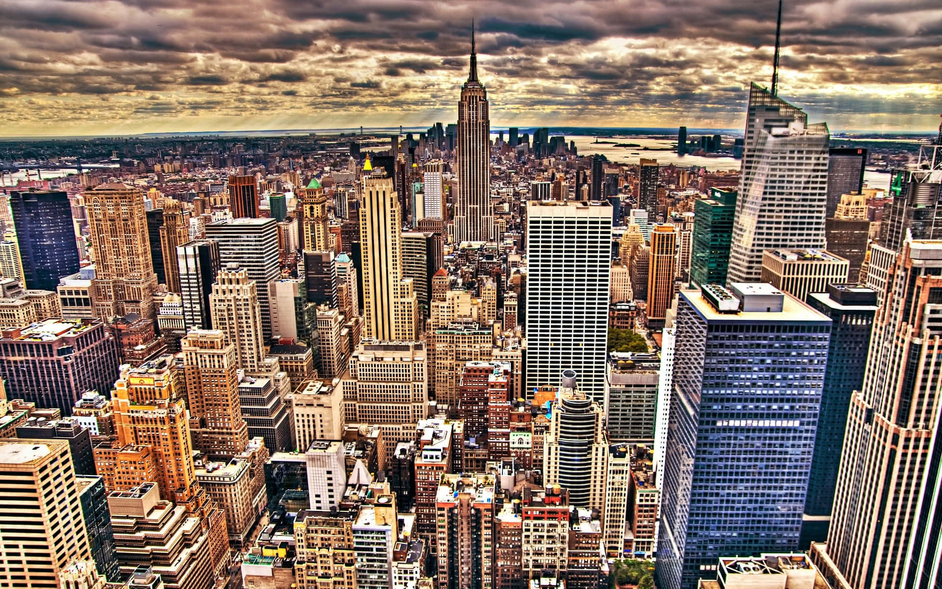 New York State 桌布 壁紙 — 紐約市天際線的鳥瞰圖，帝國大廈在戲劇性的多雲天空下聳立於密集的摩天大樓之上。