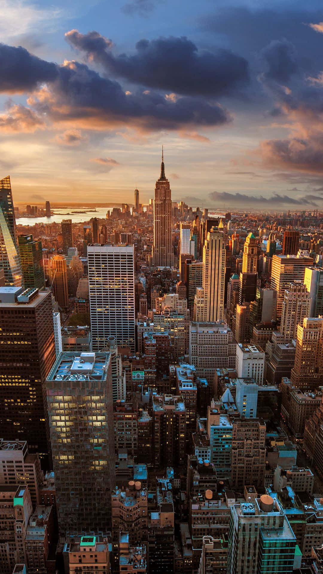 Android Ny City 桌布 壁紙 — 紐約市天際線的鳥瞰圖，日落時分，帝國大廈聳立在密集的摩天大樓之上，天空佈滿戲劇性的橙色和紫色雲彩。