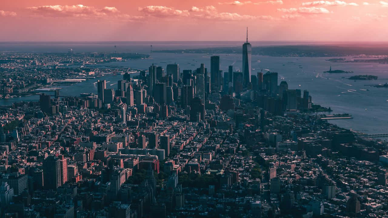 720p Empire State Building 桌布 壁紙 — 紐約市天際線的鳥瞰圖，日落時分，粉紅色的雲彩和變暗的摩天大樓倒映在水面上。