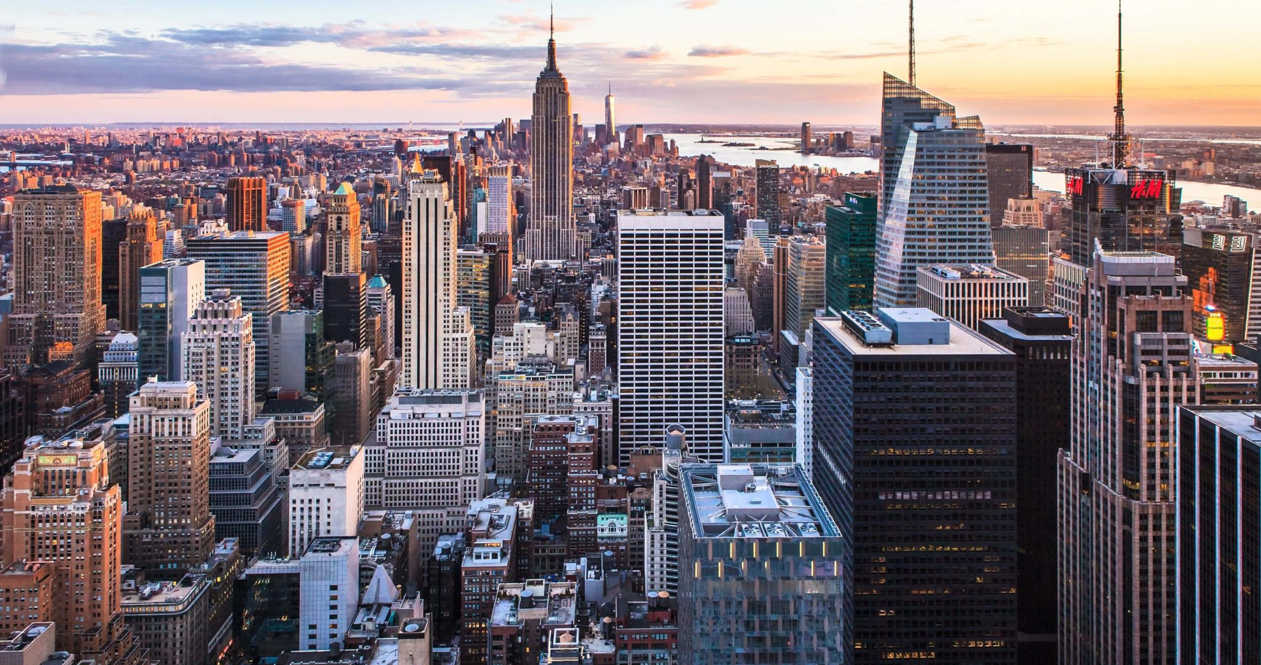 New York City 4K Ultra HD 桌布 壁紙 — 紐約市天際線的鳥瞰圖，日落時金色光芒照亮摩天大樓和遠處的水面。