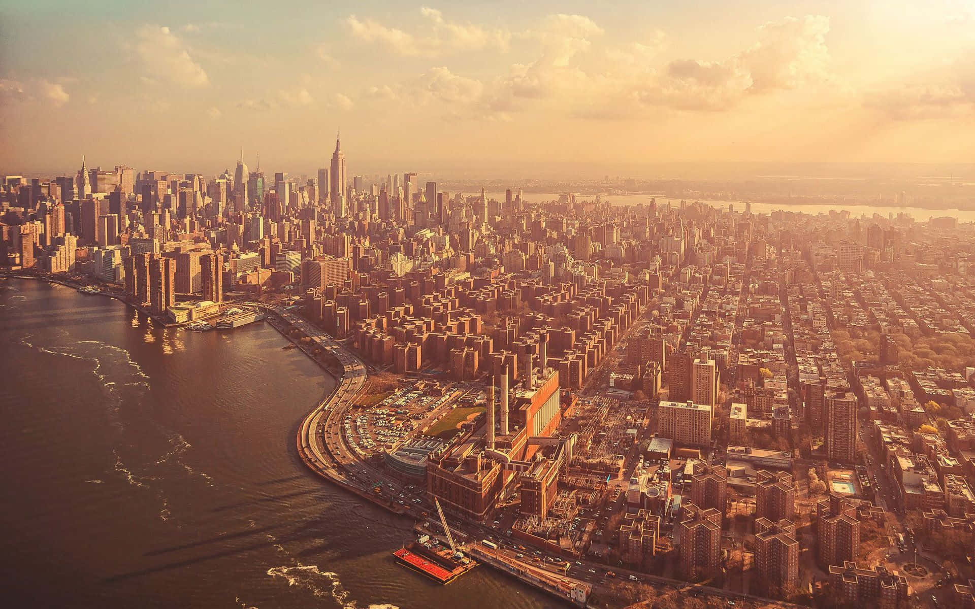 New York 桌布 壁紙 — 紐約市天際線的鳥瞰圖，沐浴在金黃色的日落光芒中，下方有雲彩和河流。