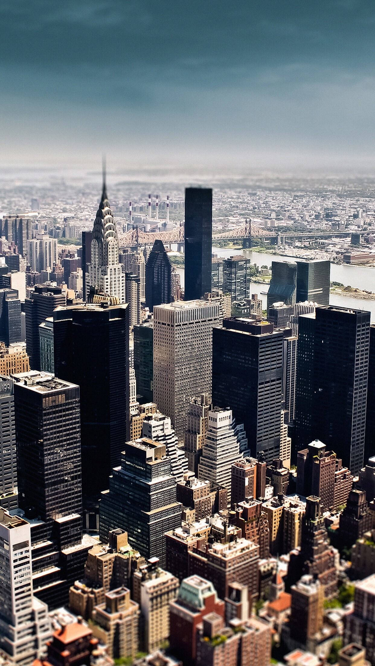 new york city iPhone x 桌布 壁紙 — 紐約市天際線的鳥瞰圖，高聳的摩天大樓和橋樑在陰沉多雲的天空下。