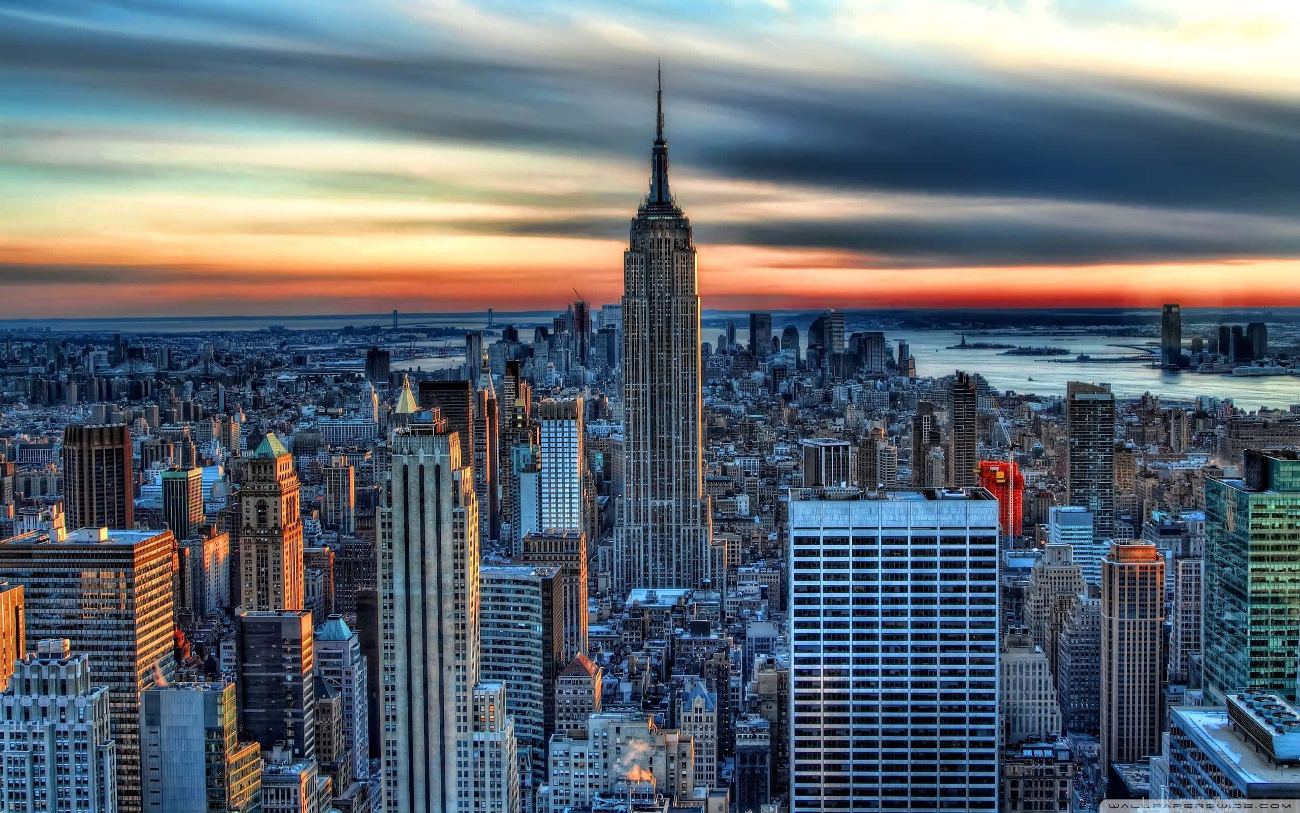New York State 桌布 壁紙 — 紐約市日落時分的全景視野，帝國大廈在條紋雲層下聳立於密集的天際線之上。