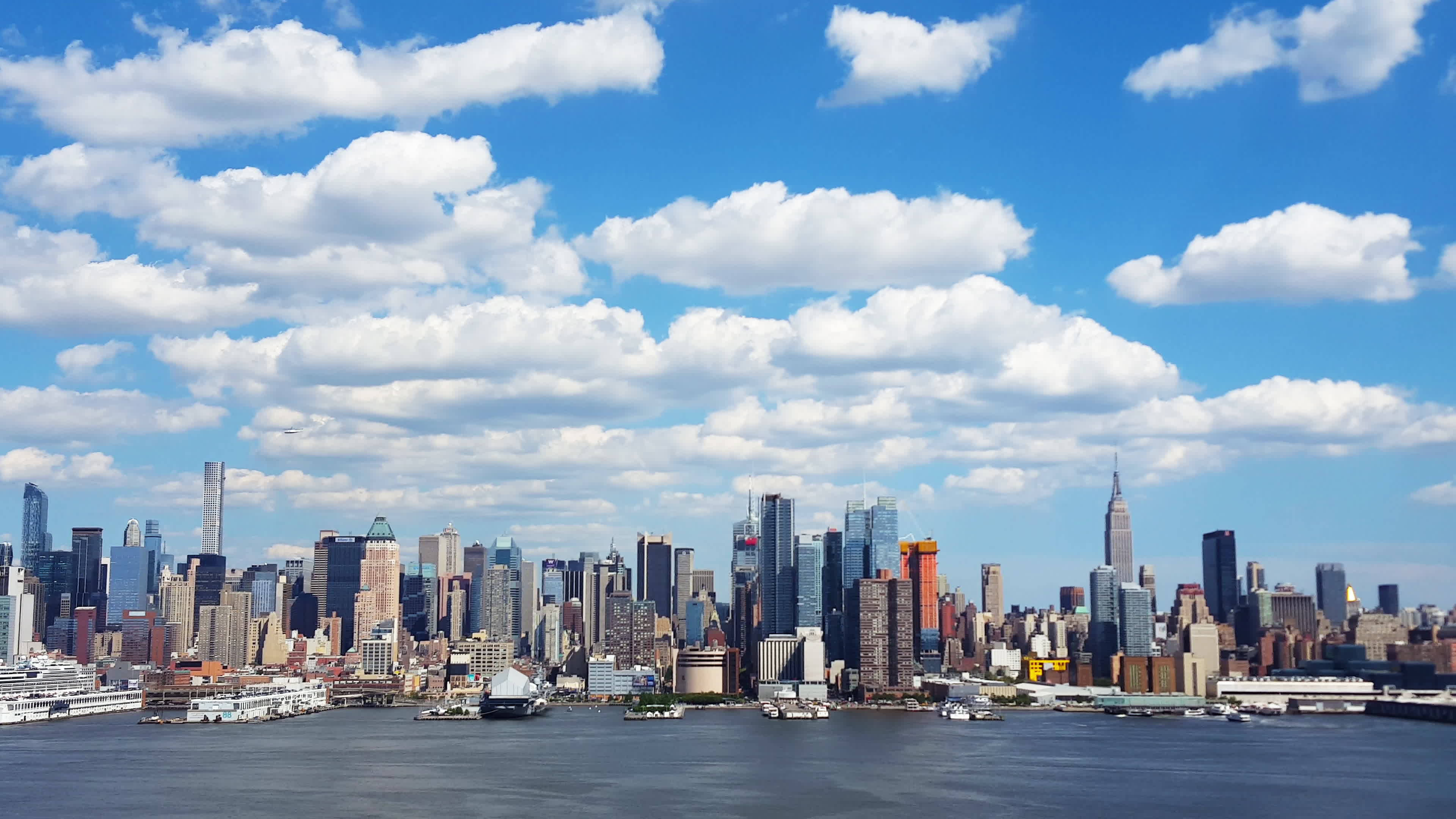 Clouds Aesthetics 桌布 壁紙 — 紐約市標誌性天際線的全景，在明亮的藍天下點綴著蓬鬆的白雲。