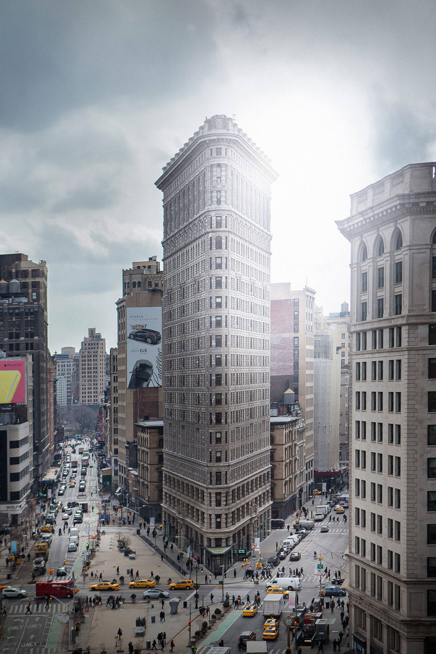 Flatiron Building 桌布 壁紙 — 紐約市標誌性的熨斗大廈在陰天的天空下巍然聳立，下方繁忙的街道上擠滿了黃色的士和行人。