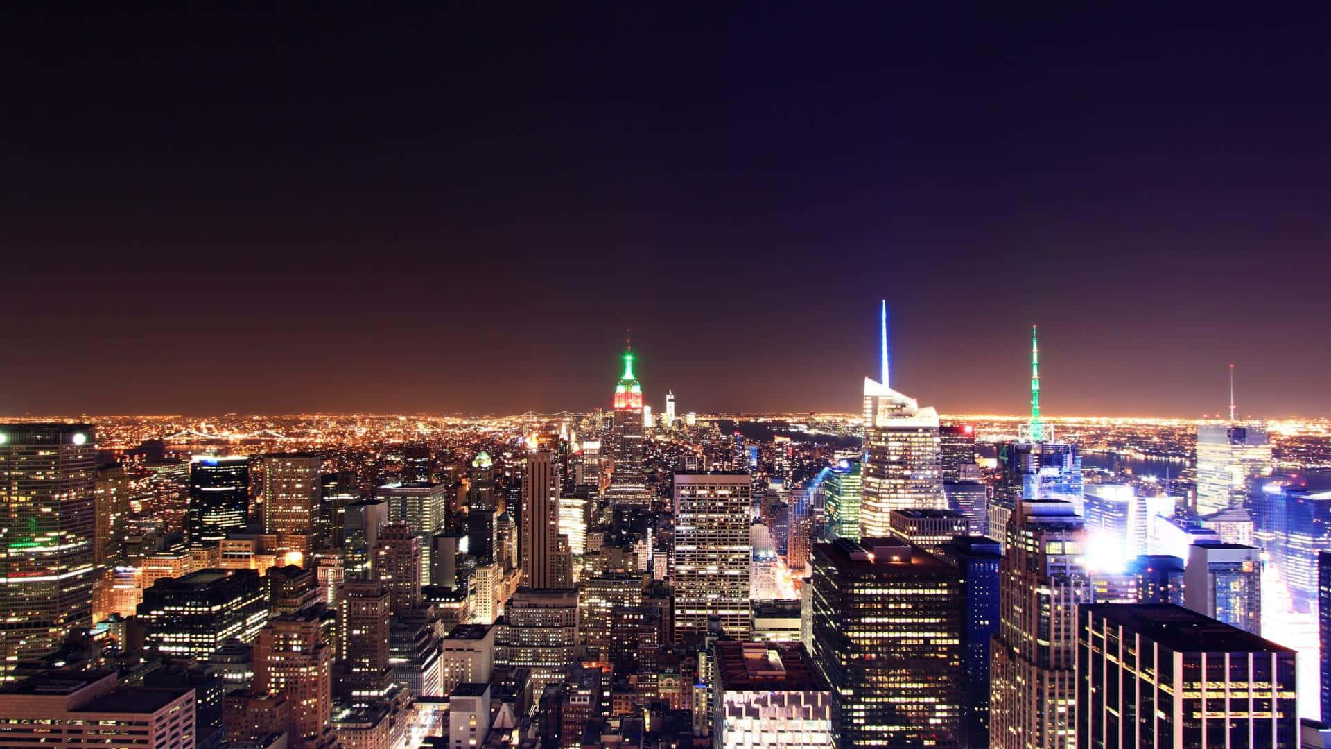 New York 桌布 壁紙 — 紐約市璀璨夜景的鳥瞰圖，標誌性摩天大樓在深紫色天空下閃耀。