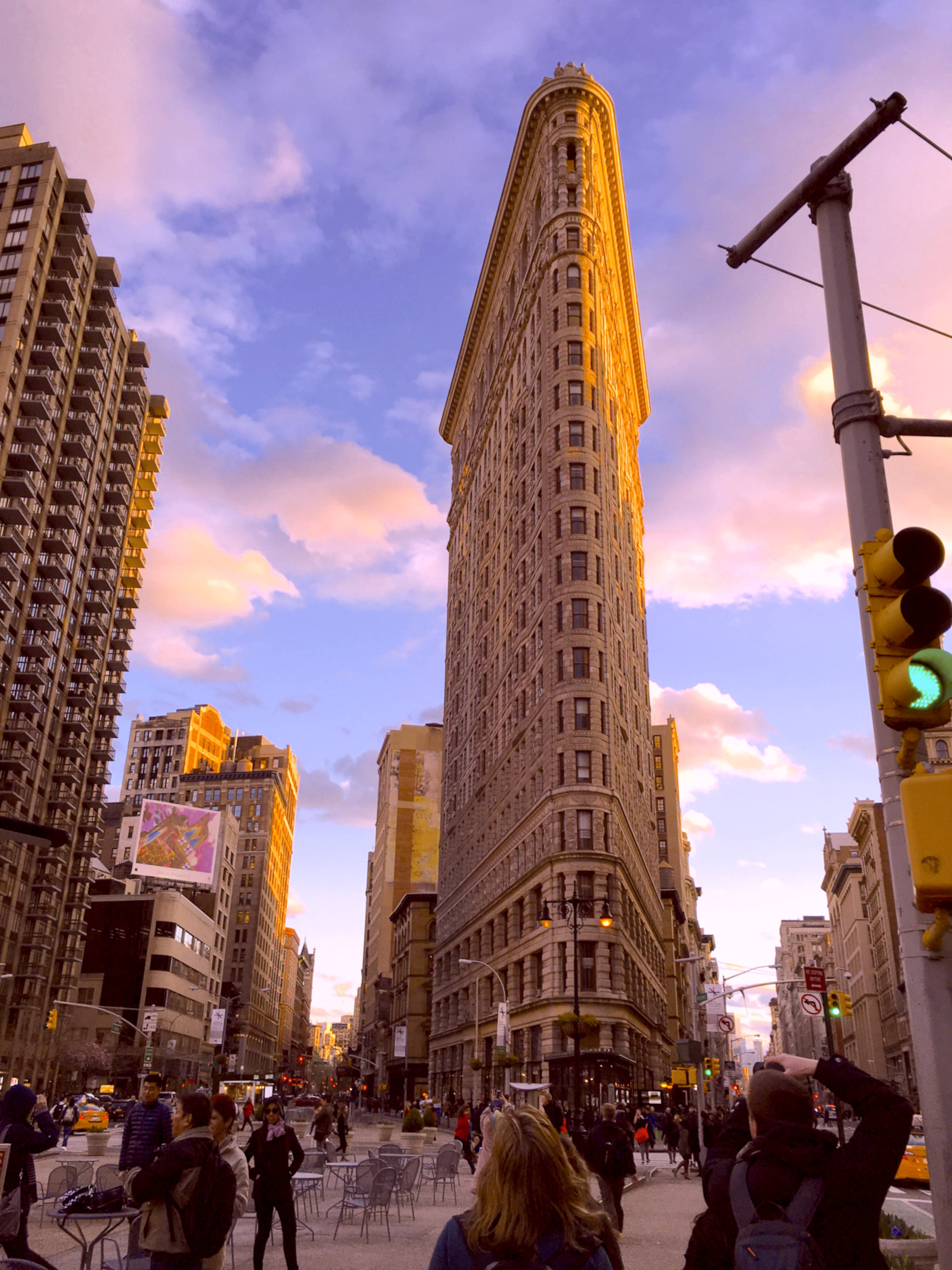 Flatiron Building 桌布 壁紙 — 紐約市的熨斗大廈在 vibrant 的日落天空下高聳矗立，行人穿梭於繁忙的城市廣場。