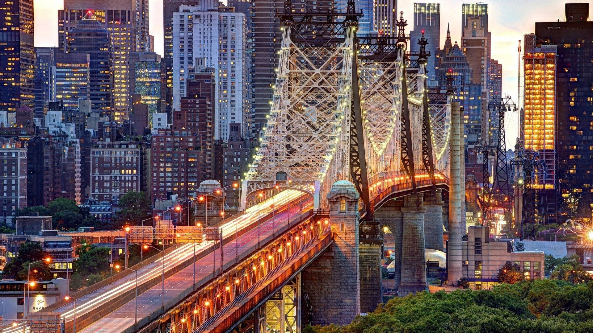 Buildings 桌布 壁紙 — 紐約市皇后區大橋在黃昏時的壯麗景色，帶有車流的光軌和燈火通明的摩天大樓。