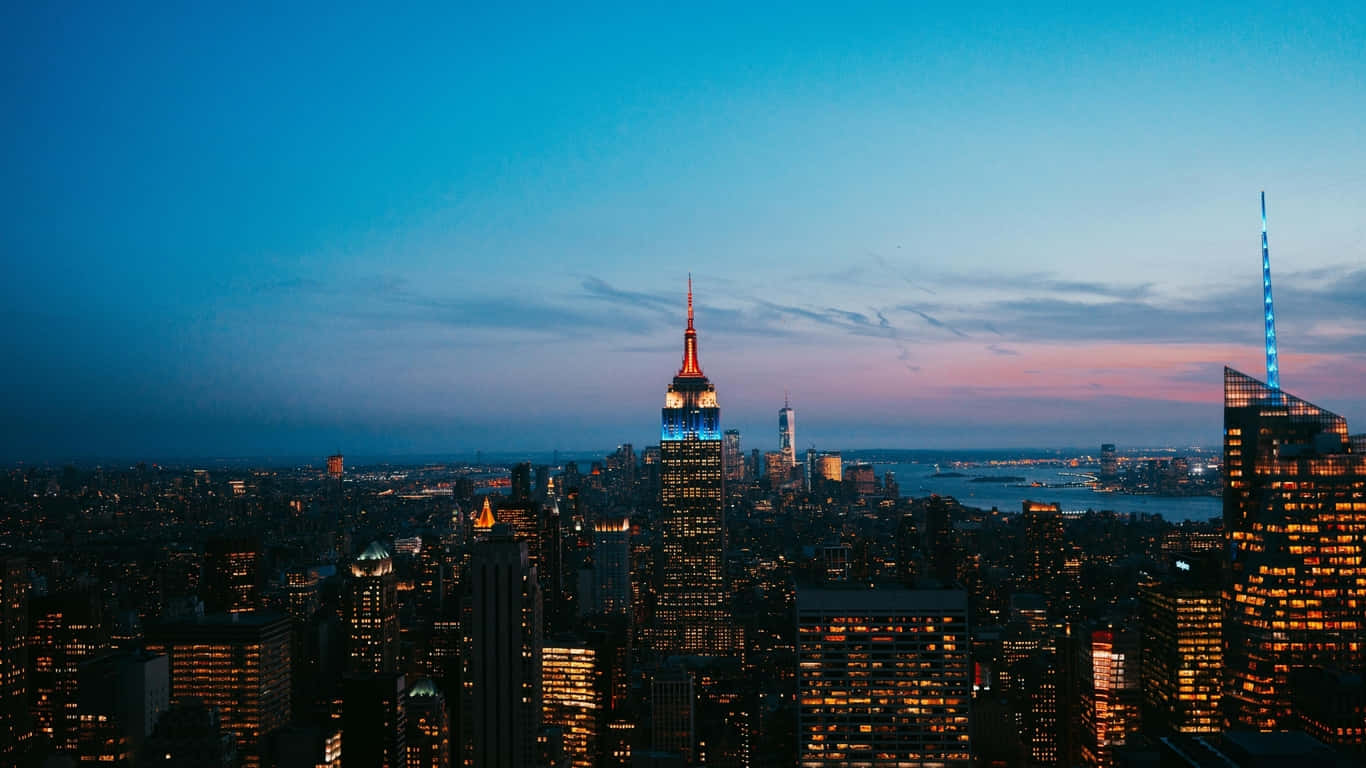 1366x768 Empire State Building 桌布 壁紙 — 紐約市黃昏時分天際線，帝國大廈在藍粉漸變的天空中閃耀。