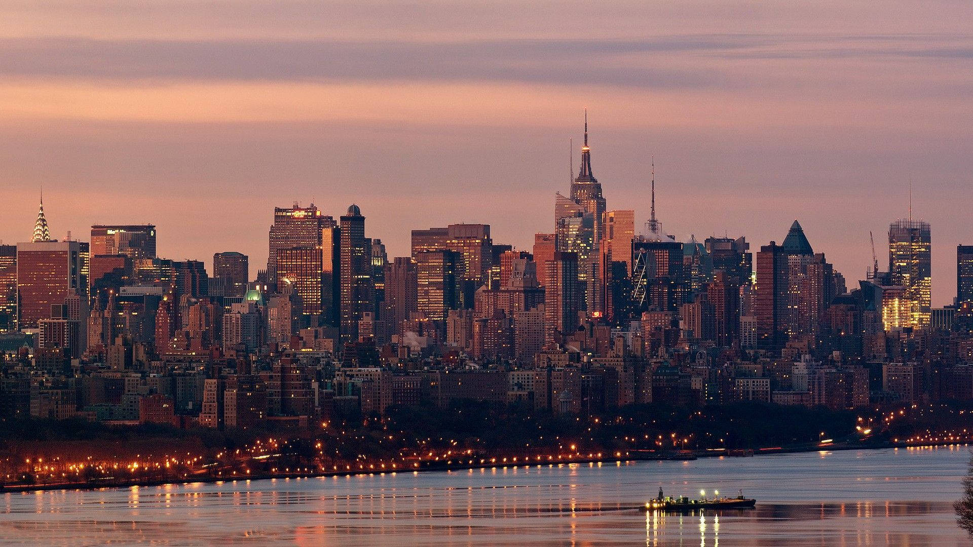 New York Skyline 桌布 壁紙 — 紐約市黃昏時分天際線，發光的摩天大樓倒映在下面的河流中。