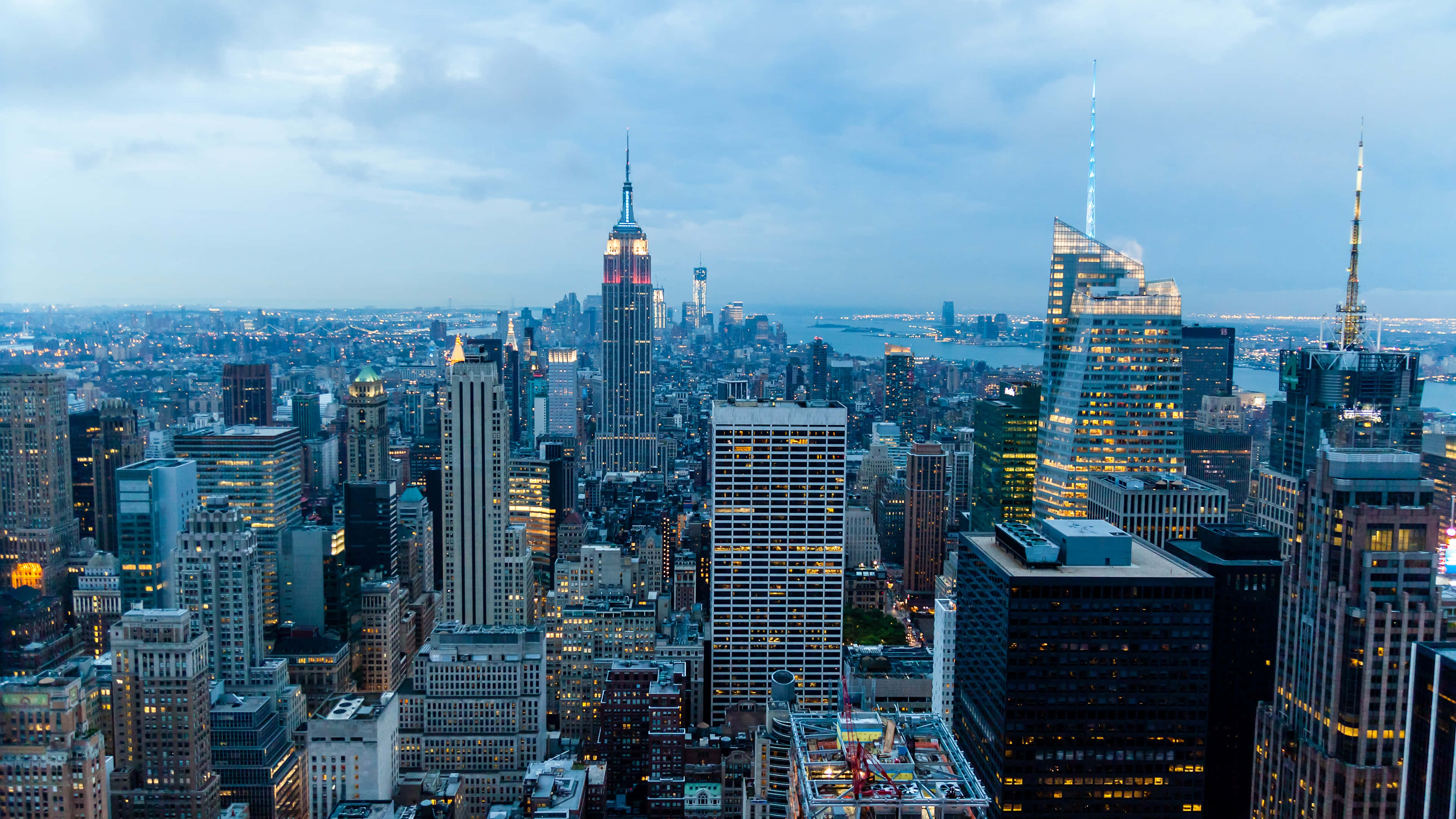 New York City 4K Ultra HD 桌布 壁紙 — 紐約市黃昏時分的全景，摩天大樓在陰雲密布的天空下亮起燈光。