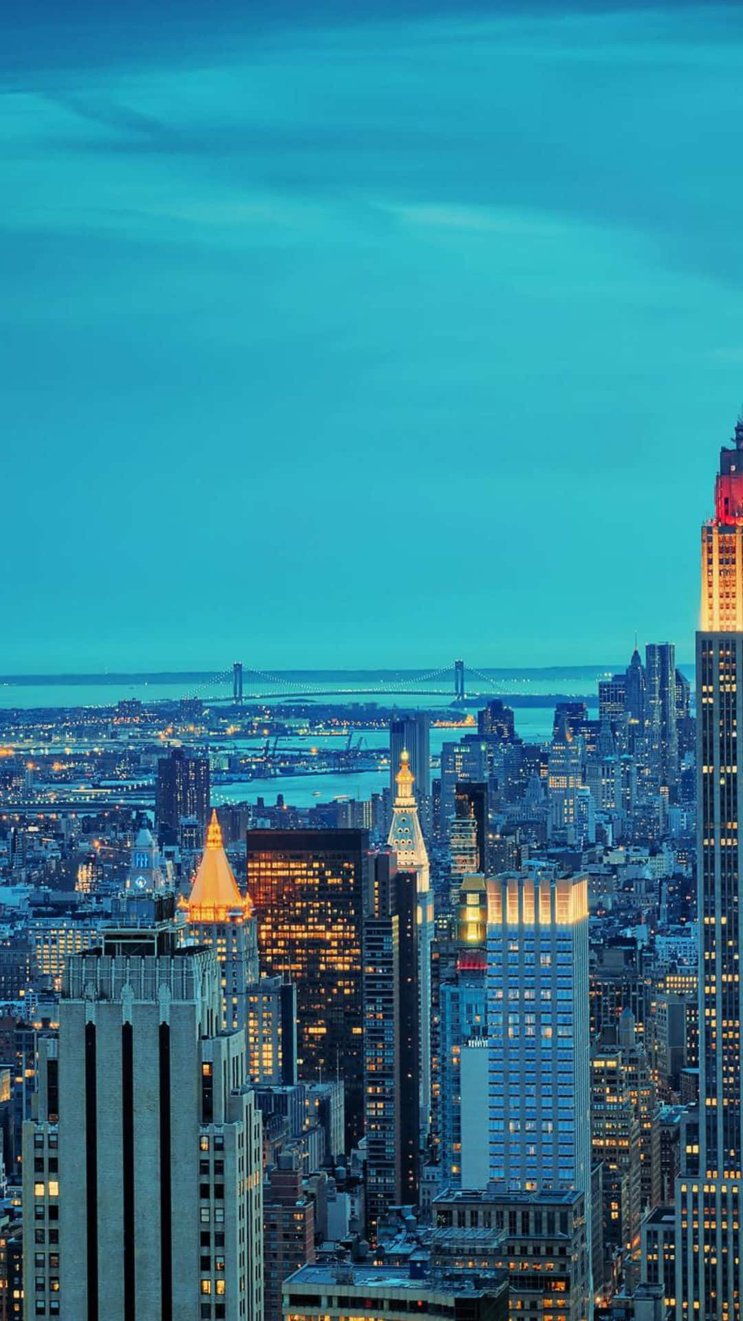 Android Ny City 桌布 壁紙 — 紐約市黃昏時分的全景，閃爍的摩天大樓和一座橫跨水面的橋樑，在深藍色的天空下。