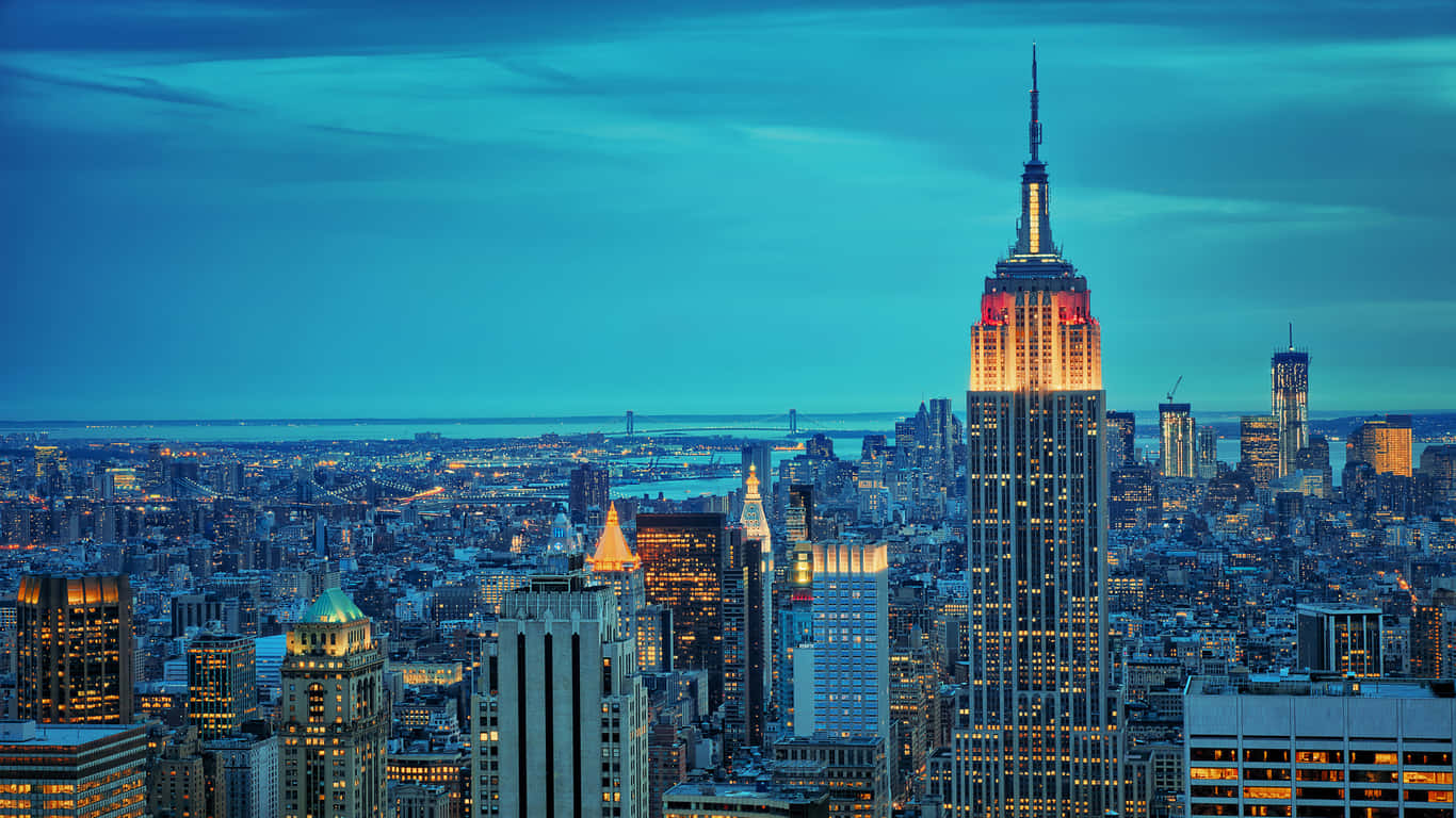 1366x768 Empire State Building 桌布 壁紙 — 紐約市黃昏時分的全景視圖，帝國大廈在深藍色天空的映襯下閃耀。