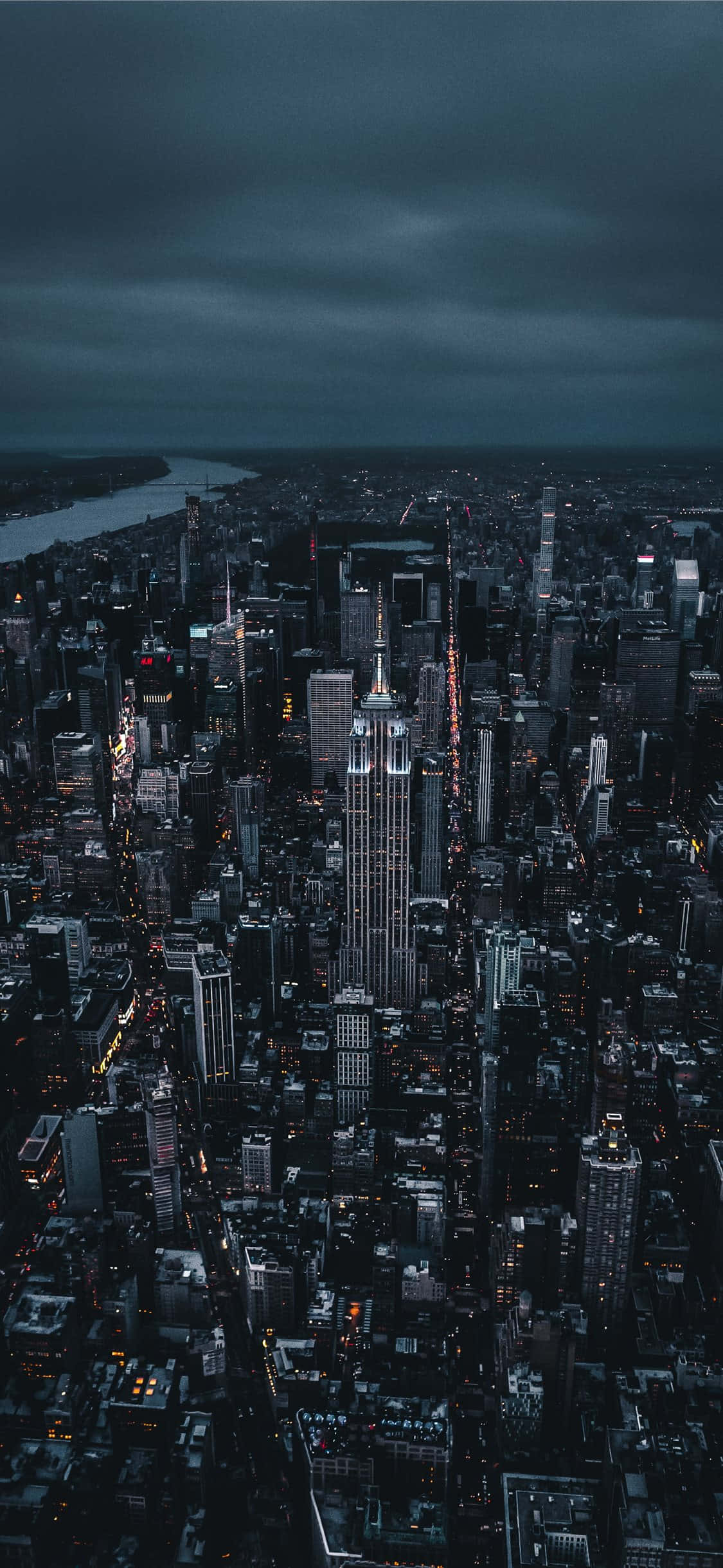 iPhone Xs New York 桌布 壁紙 — 紐約市黃昏時分的陰鬱空拍圖，帝國大廈在黑暗多雲的天空中亮起燈光。