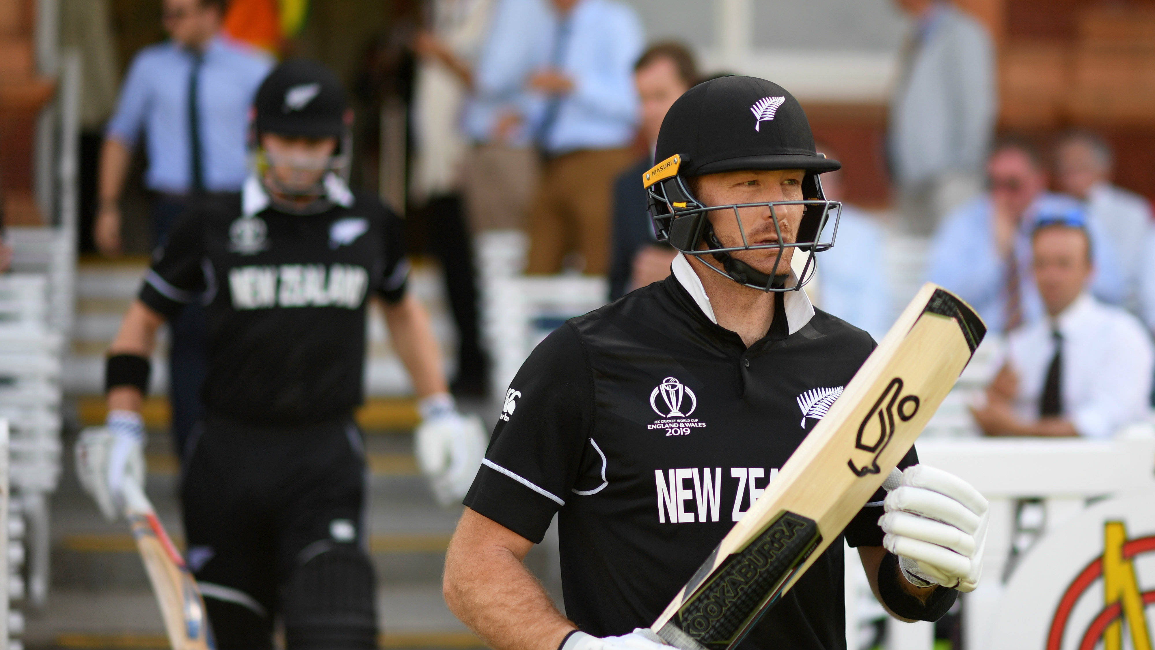 martin guptill 桌布 壁紙 — 紐西蘭板球球員身穿黑色制服手持球棒，在日間比賽中自信地走在球場上。
