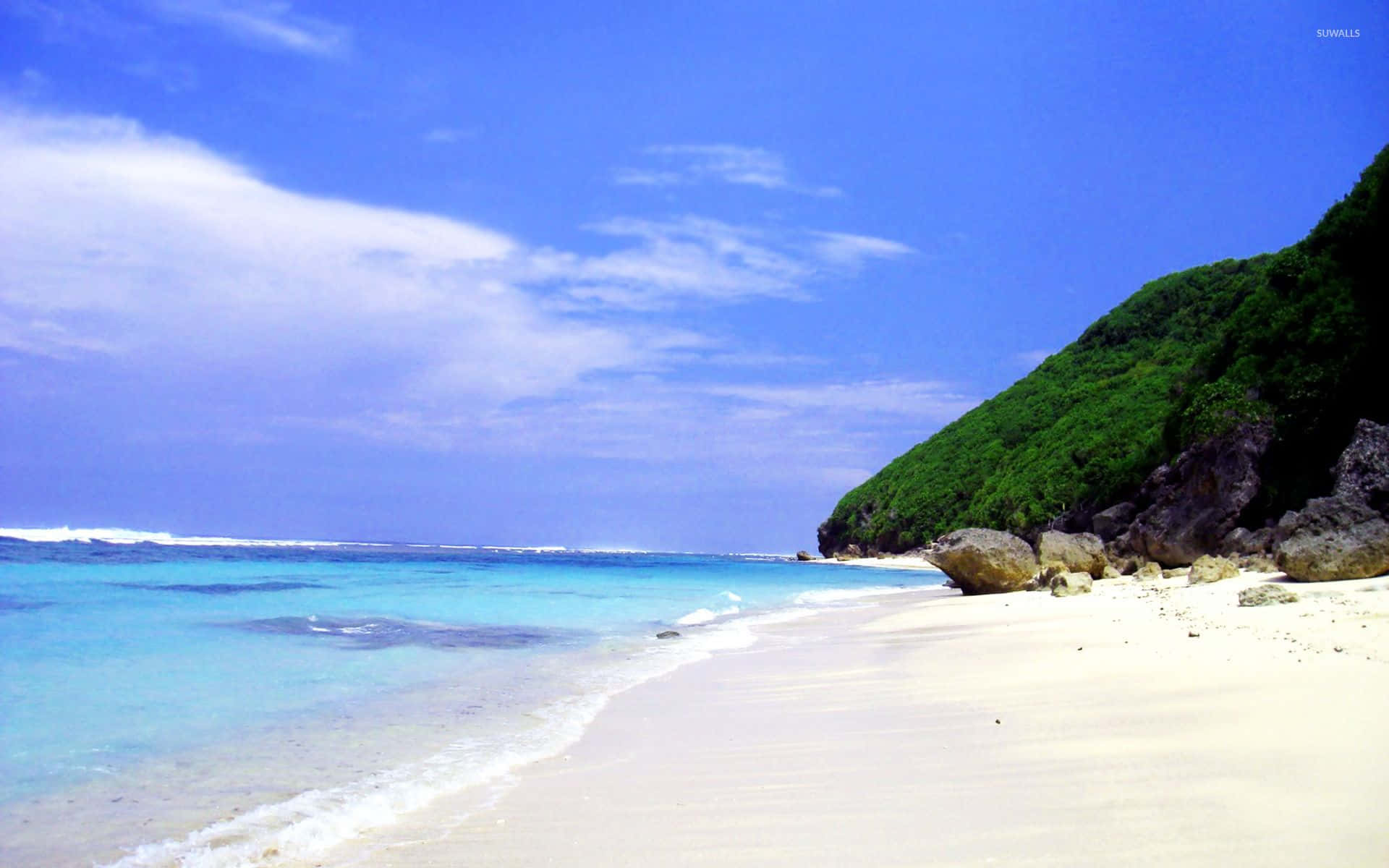 Bali Beach 桌布 壁紙 — 純淨的白色沙灘沿著碧綠的海水蜿蜒伸展，上方是藍天白雲。