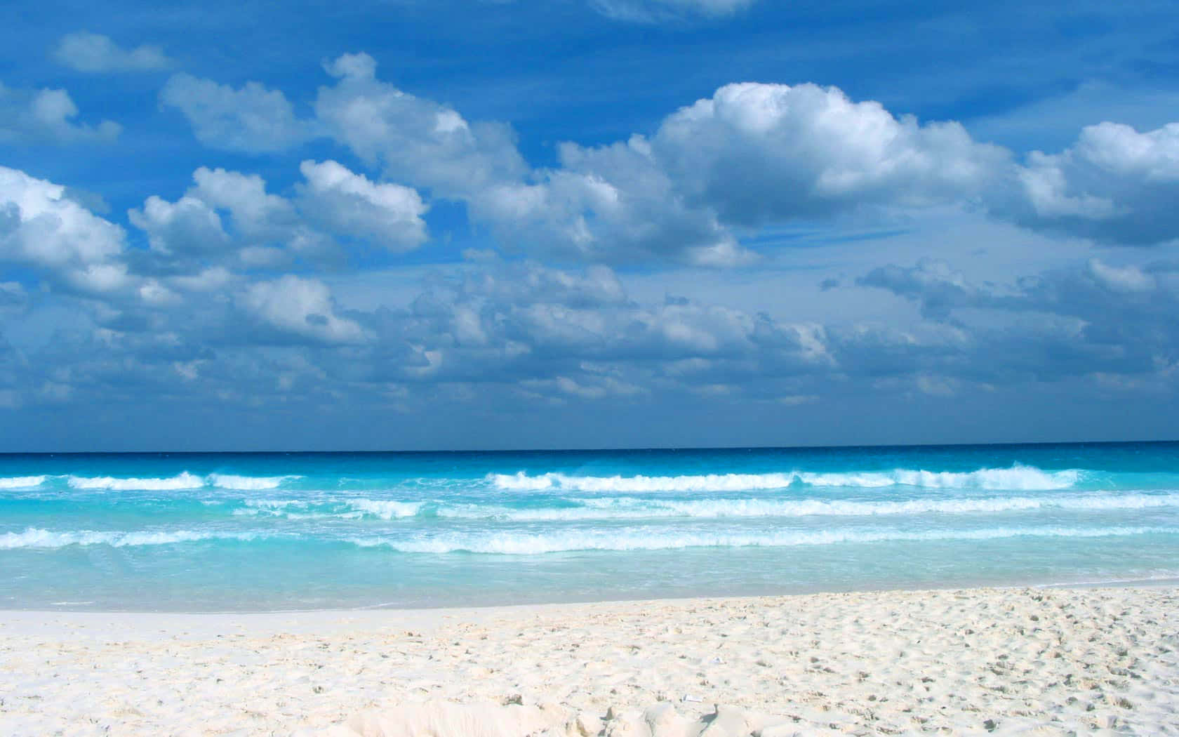Caribbean Beach 桌布 壁紙 — 純淨的白色沙灘與碧綠的海浪相遇，在廣闊的藍天下點綴著蓬鬆的白雲。