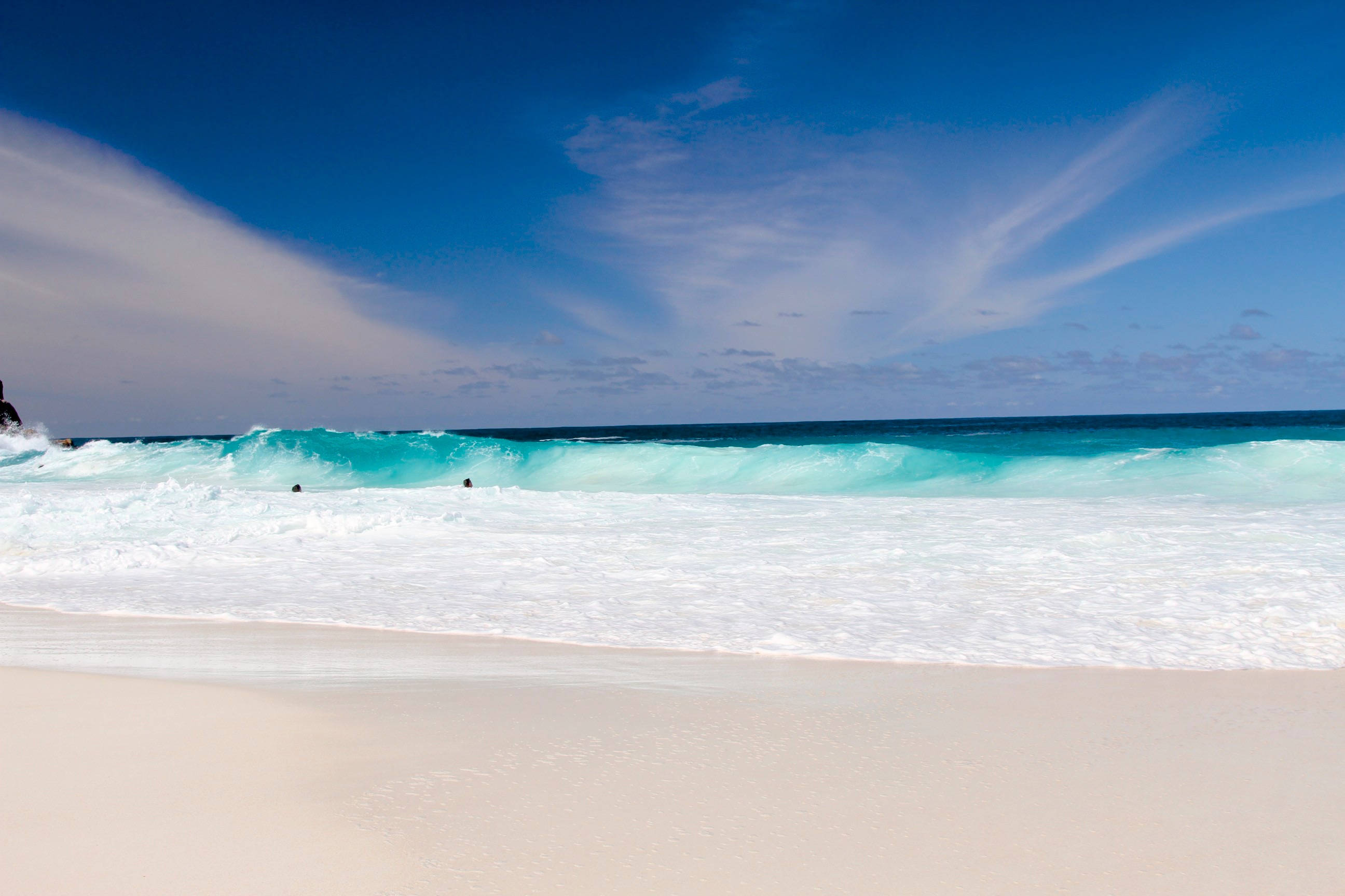 Seychelles 桌布 壁紙 — 純淨的白色沙灘與碧綠的海浪相遇，在廣闊的藍天和縷縷白雲下。