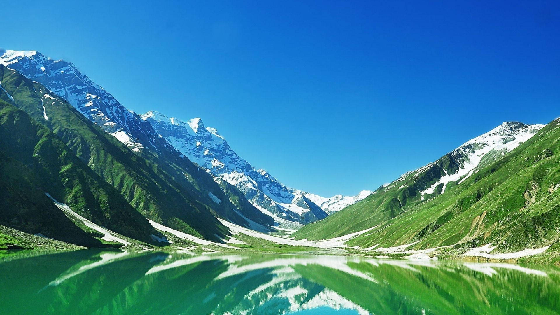 Pakistan 桌布 壁紙 — 純淨的高山湖泊倒映著白雪覆蓋的山峰，藍天白雲下，四周環繞著鬱鬱蔥蔥的綠色山坡。