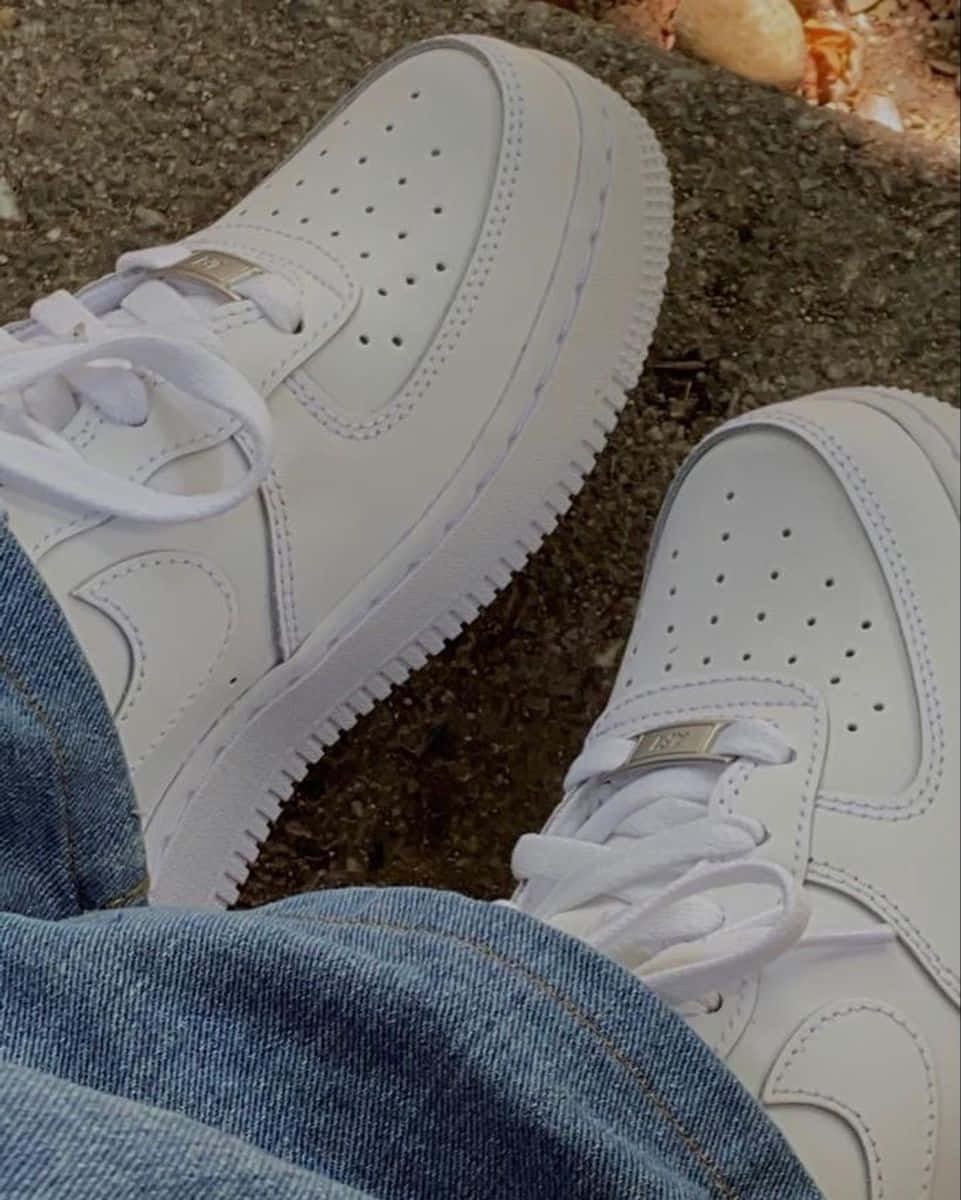 Nike Air Force 桌布 壁紙 — 純白Nike Air Force 1運動鞋搭配藍色牛仔褲的特寫，地面有紋理。