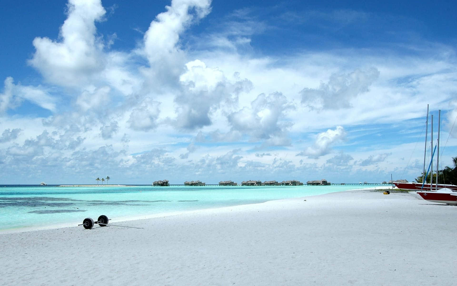 Maldives Beach 桌布 壁紙 — 純白沙灘、碧綠海水、水上小屋，在晴朗藍天與蓬鬆白雲下。