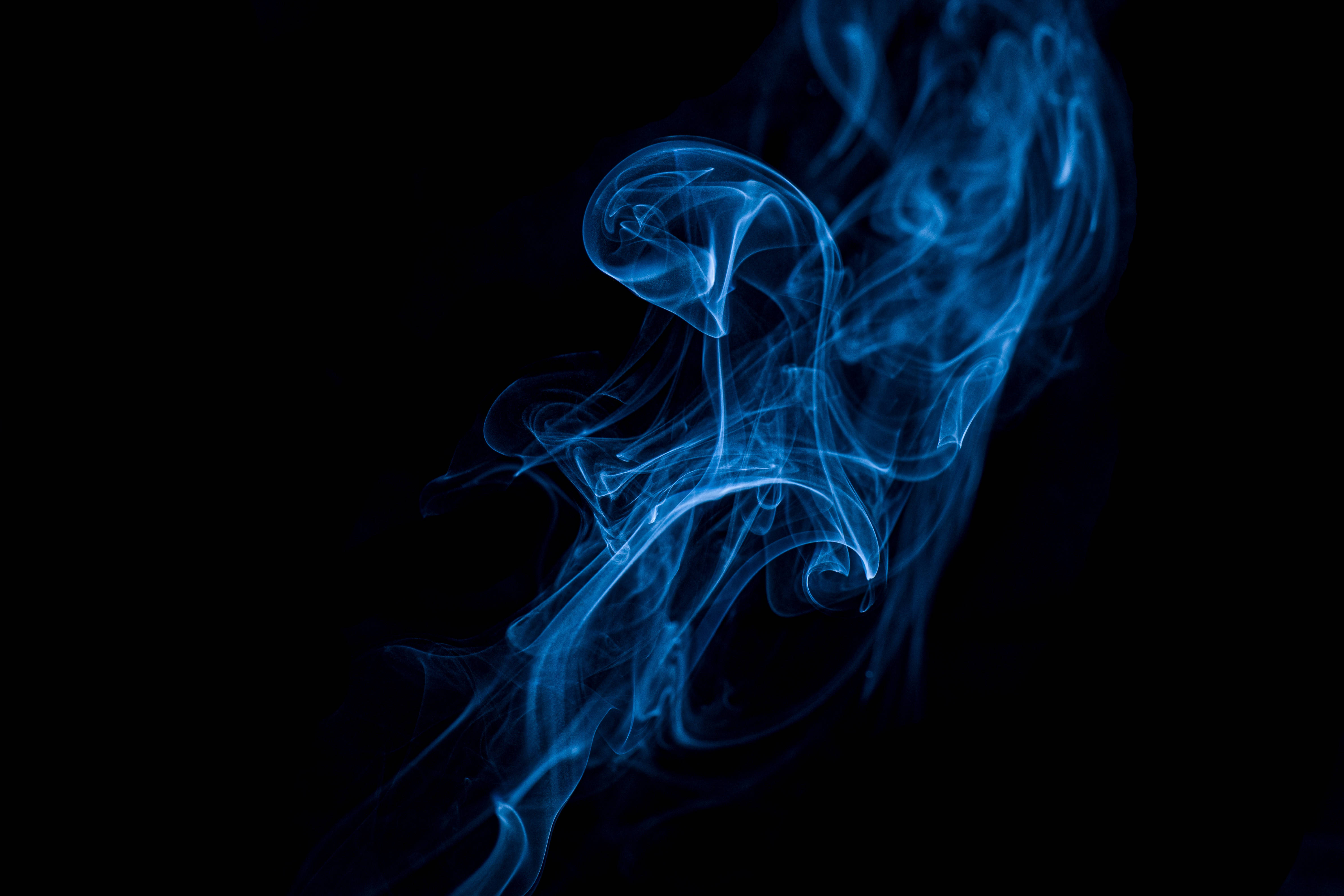 抽菸 桌布 壁紙 — 純粹黑色背景上，空靈的藍色煙霧優雅地旋轉，形成迷人的抽象形態。