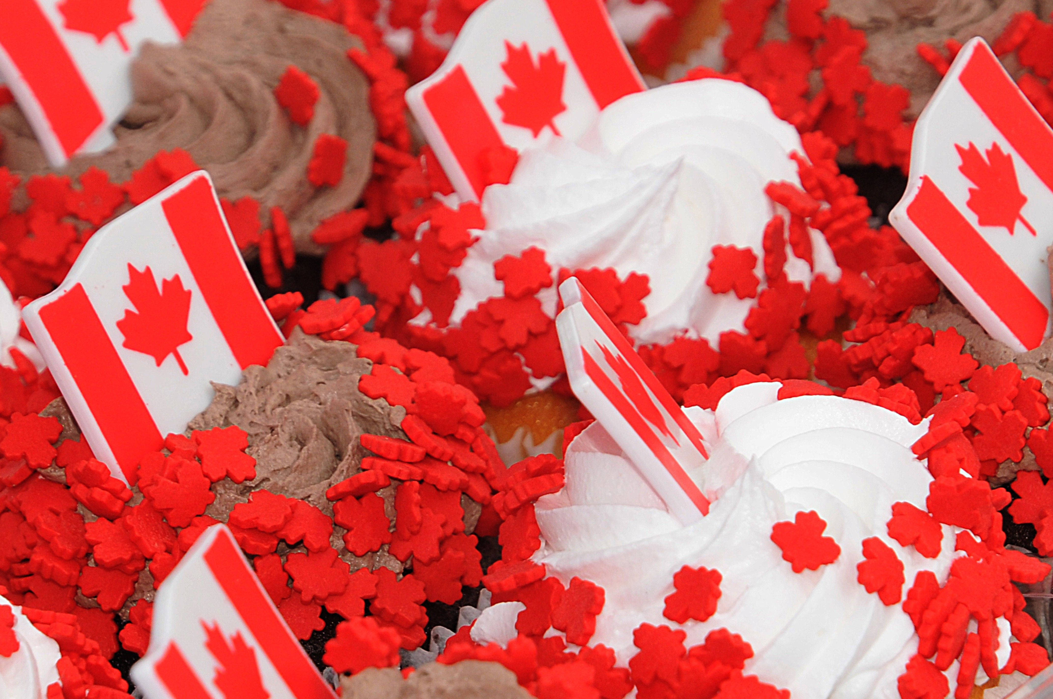 Canada Day 桌布 壁紙 — 紙杯蛋糕特寫，頂部有白色和巧克力糖霜、加拿大國旗和紅色楓葉糖粒。
