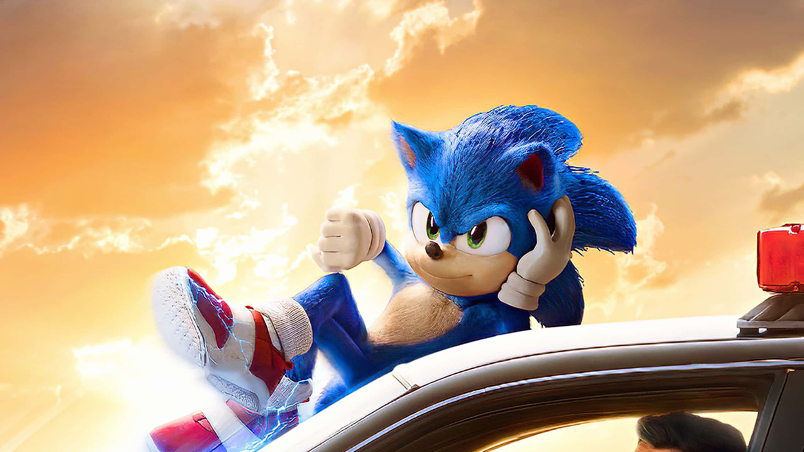 Sonic The Hedgehog 桌布 壁紙 — 索尼克躺在一輛高速行駛的車頂上，背景是金色夕陽天空和戲劇性的雲層。