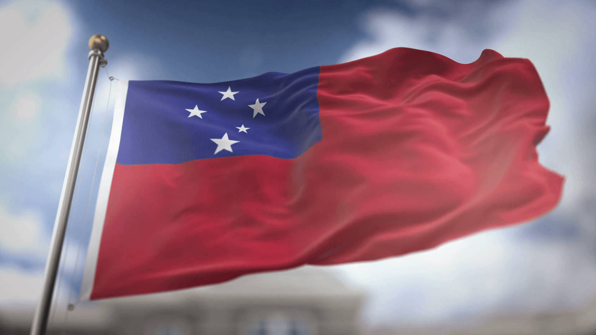 Flag 桌布 壁紙 — 索羅門群島國旗在陰天背景下動態飄揚，背景有模糊的建築物。