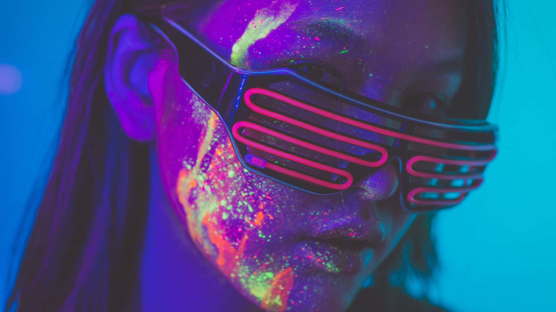 Glow In The Dark 桌布 壁紙 — 紫外光下，一個帶有發光霓虹妝容和未來感粉紅色護目鏡的人物特寫。