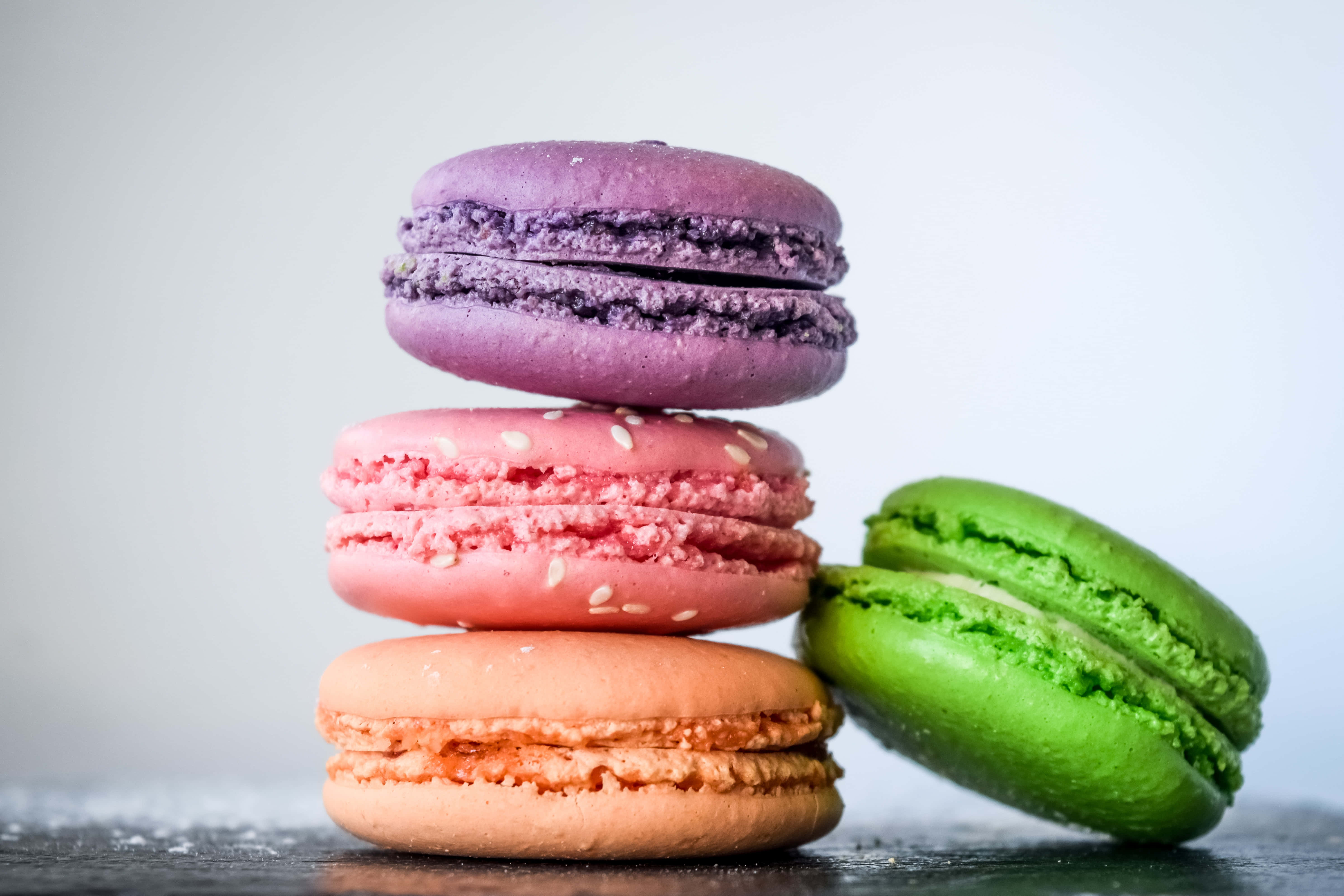 Desserts 桌布 壁紙 — 紫色、粉紅色和橙色的馬卡龍堆疊在一起，旁邊有一個綠色的馬卡龍，放在深色表面上。