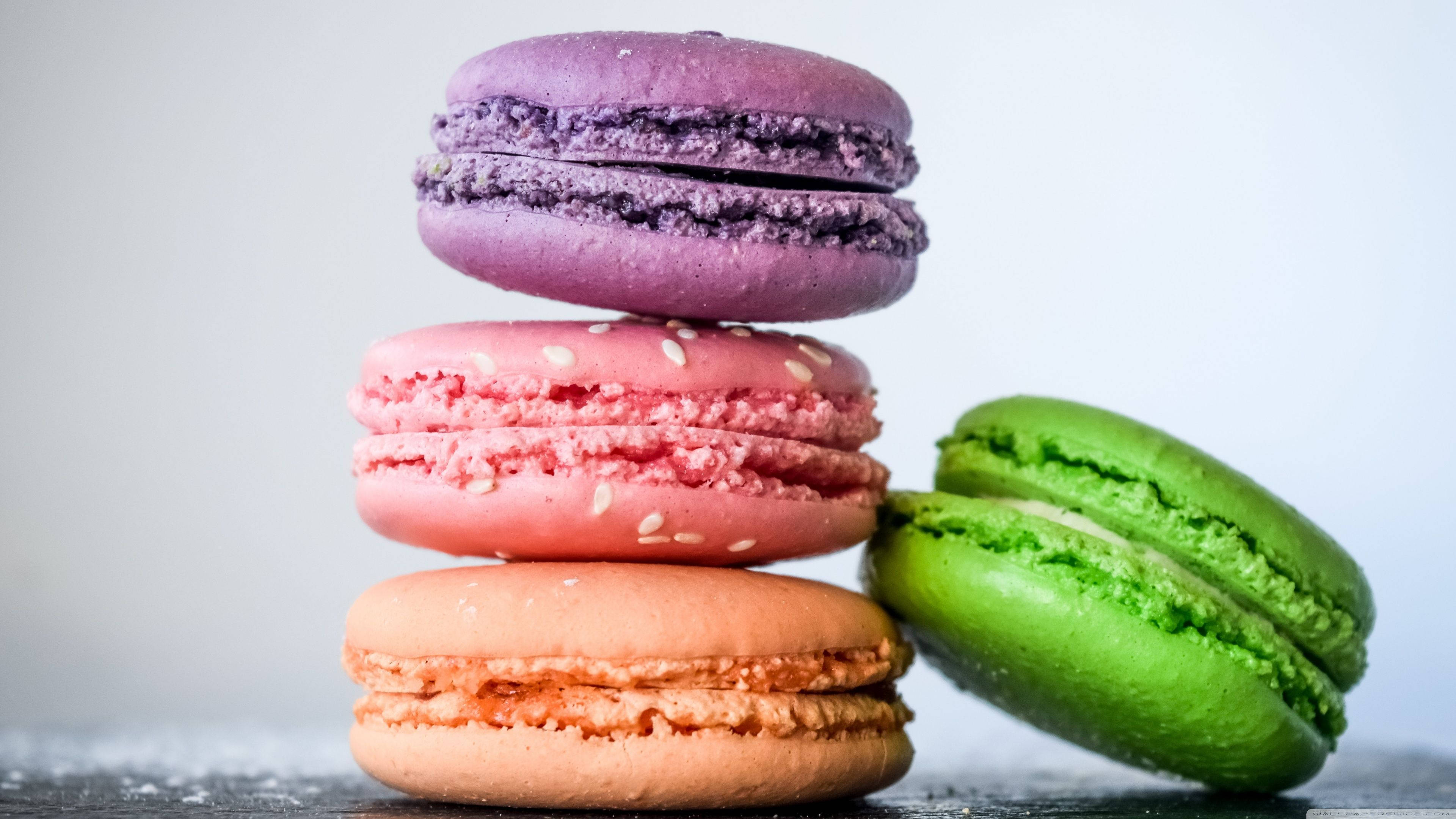 Pastry 桌布 壁紙 — 紫色、粉紅色和蜜桃色的粉彩馬卡龍堆疊在一起，旁邊有一個綠色的馬卡龍，放在深色表面上。
