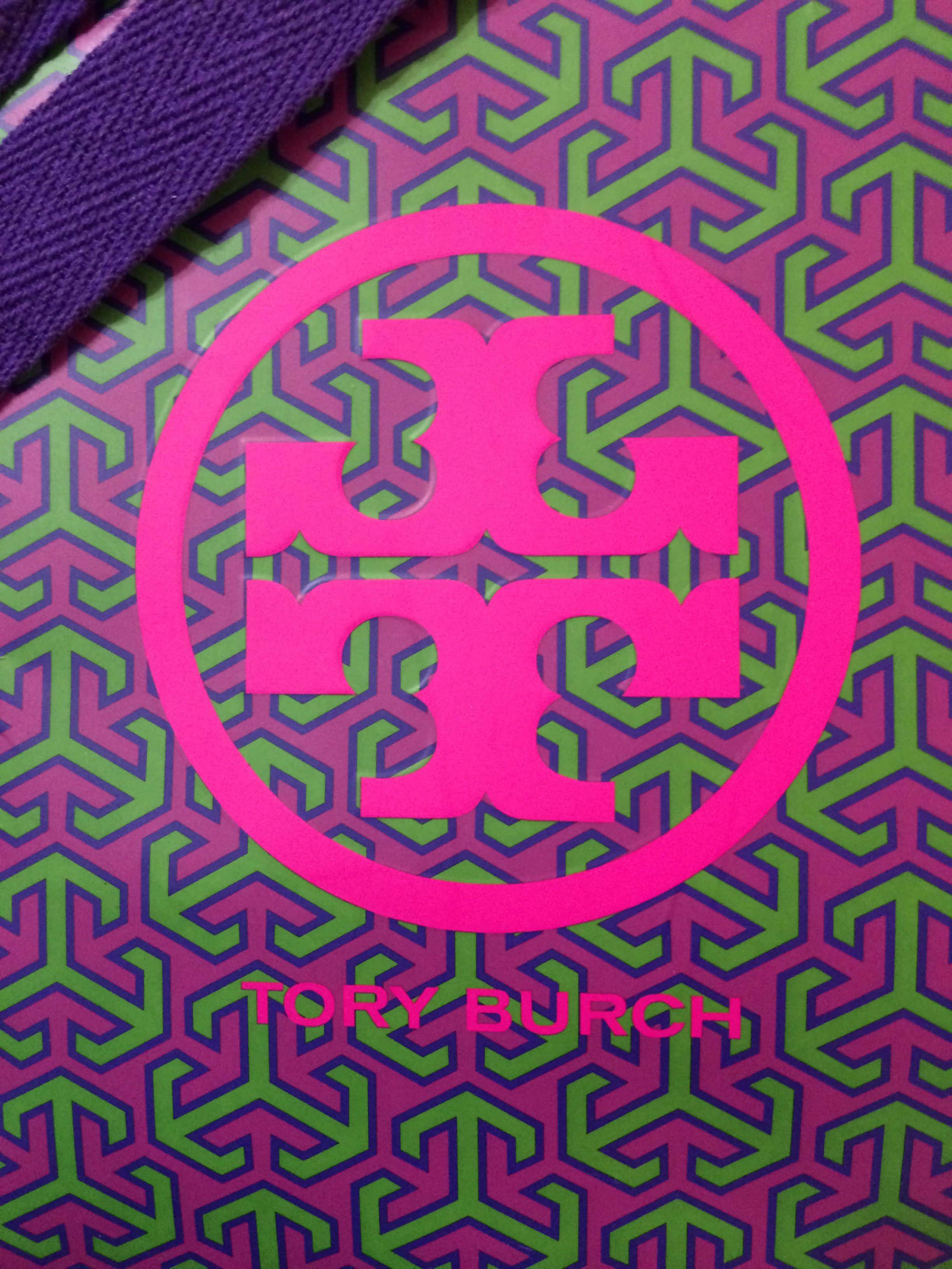 Tory Burch 桌布 壁紙 — 紫色和綠色幾何圖案手提袋上鮮豔粉紅色Tory Burch標誌的特寫。