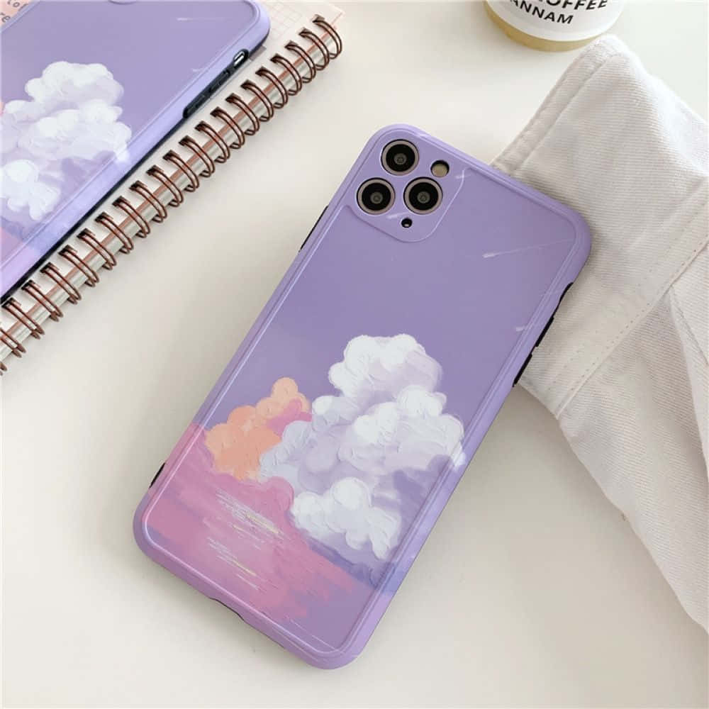 Phone Case 桌布 壁紙 — 紫色手機殼上繪有雲彩和日落色調，放在白色桌面上，旁邊有筆記本和咖啡杯。