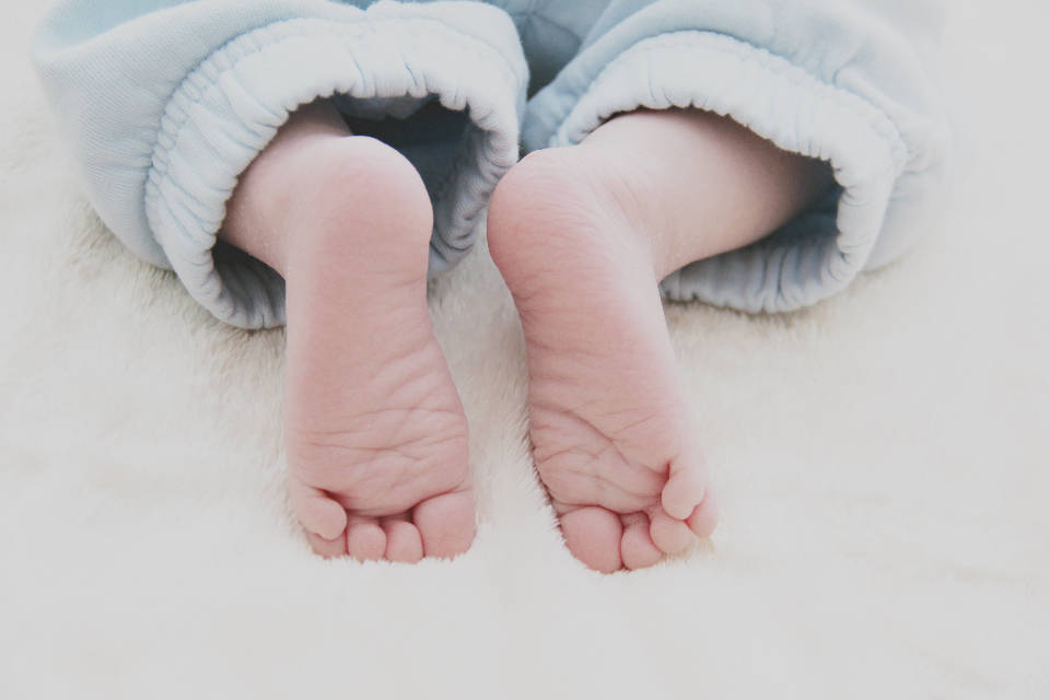Baby Boy 桌布 壁紙 — 細小的嬰兒腳從柔軟的藍色褲子中露出，放在蓬鬆的白色毯子上。