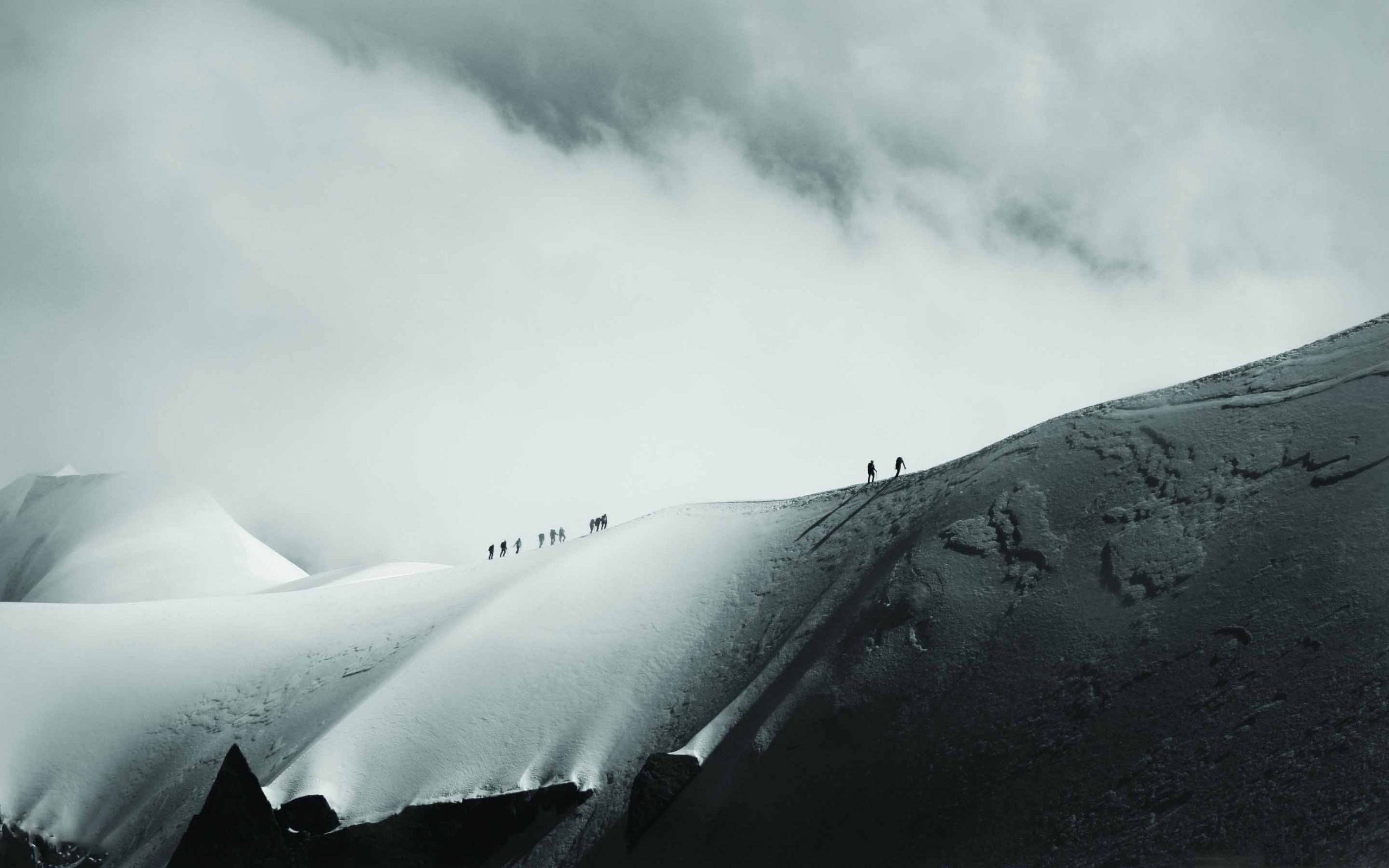 Climbing 桌布 壁紙 — 細小的攀登者在密雲天空下攀登積雪的山脊。