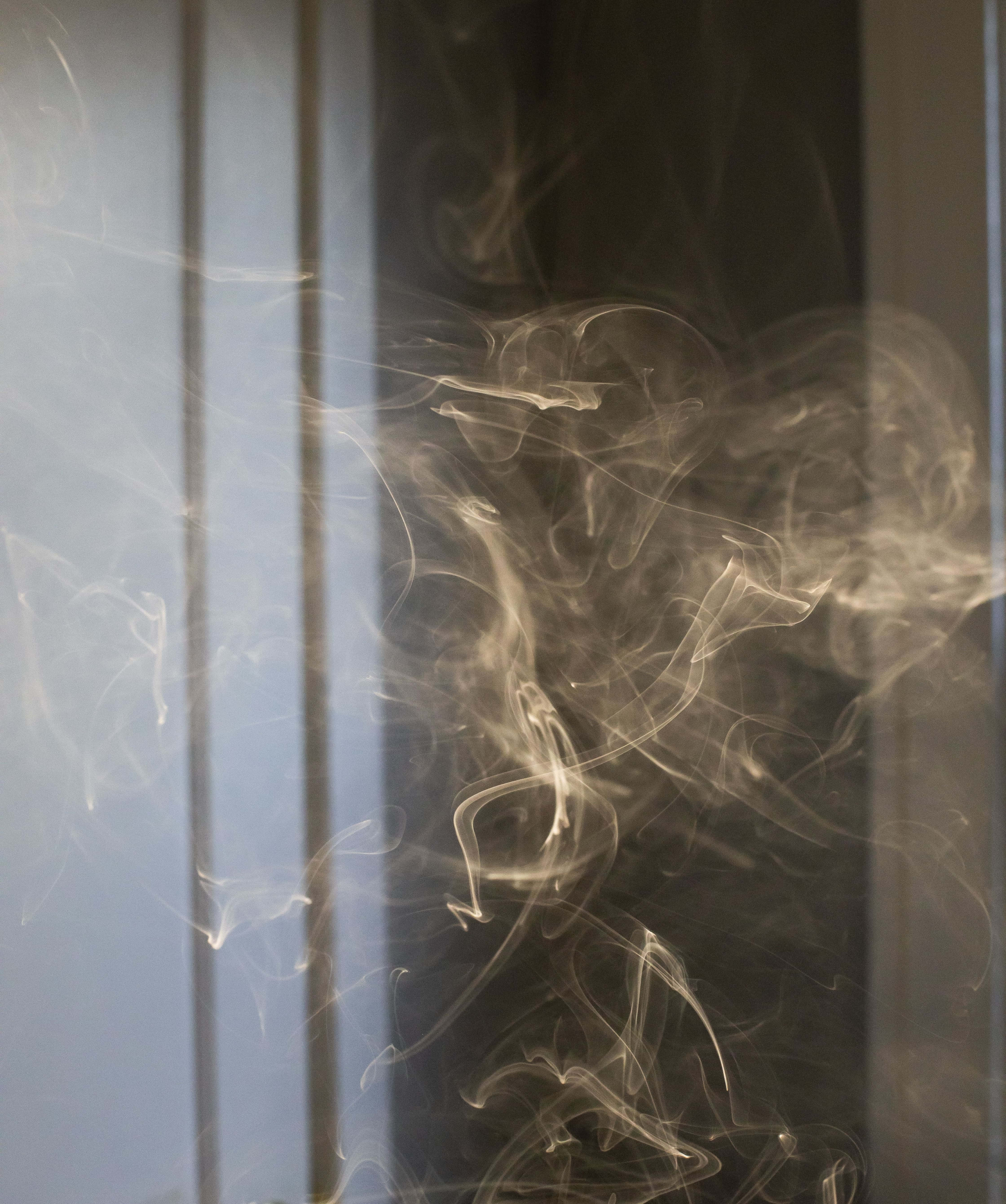 Smokey 桌布 壁紙 — 細膩的煙霧縷縷在柔和自然光下的垂直百葉窗背景中優雅地旋轉。