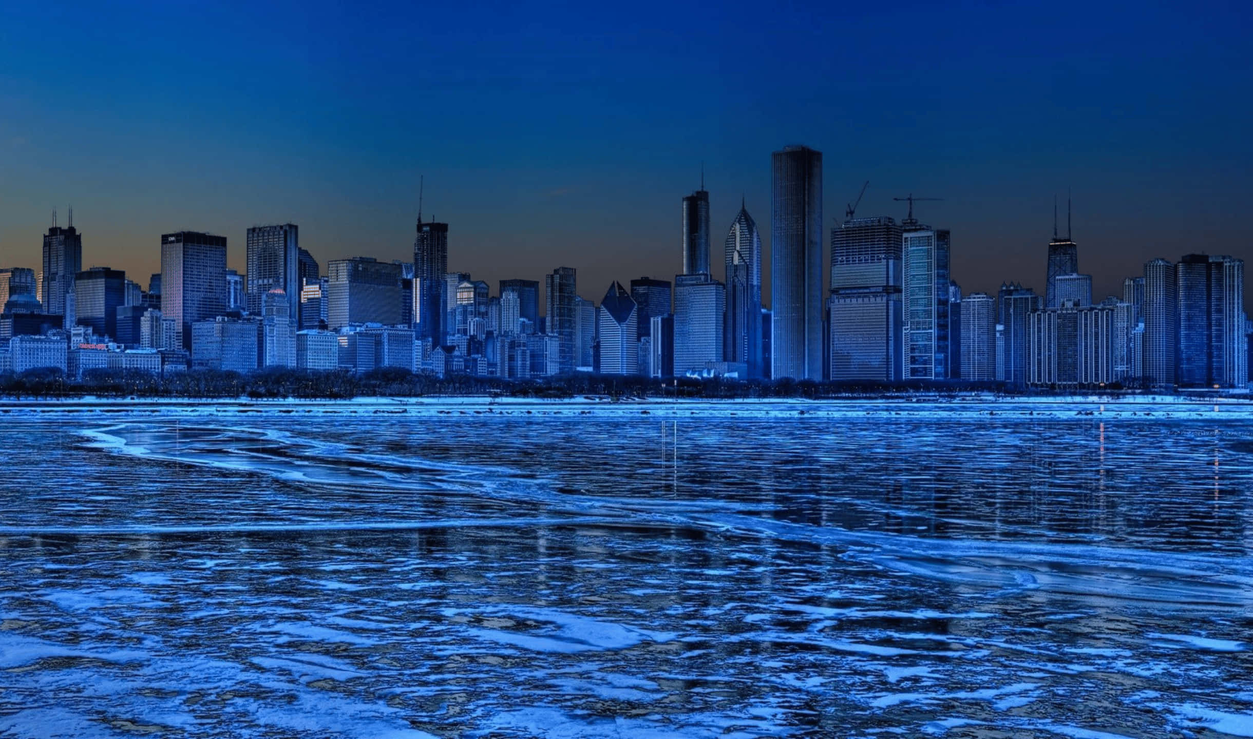 City Skyline 桌布 壁紙 — 結冰的湖面反射出冬日城市在黃昏時閃爍的藍色天際線。