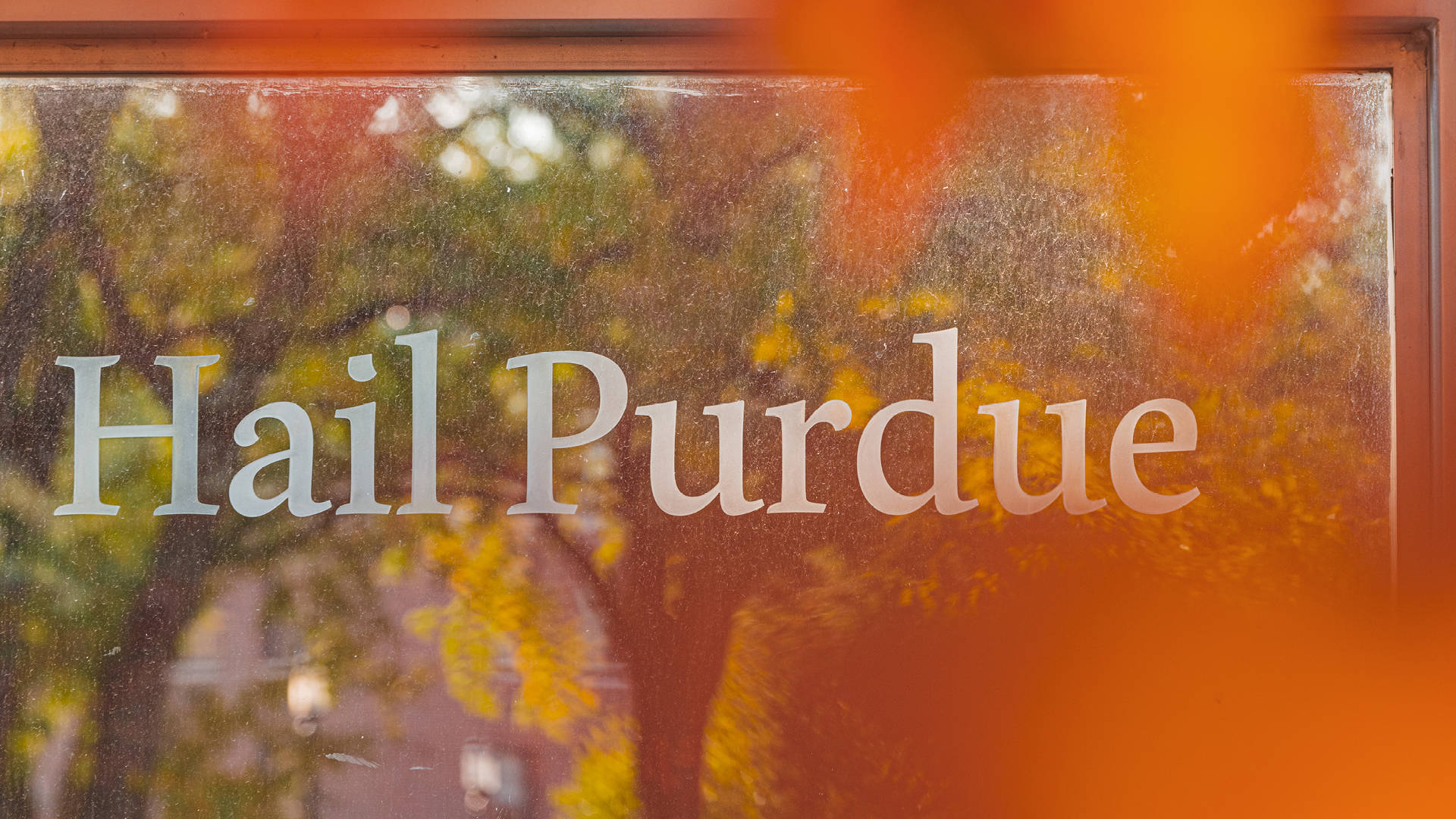 Quote 桌布 壁紙 — 結霜的窗戶顯示白色字體的「Hail Purdue」，背景是模糊的秋樹和溫暖的橙色燈光。