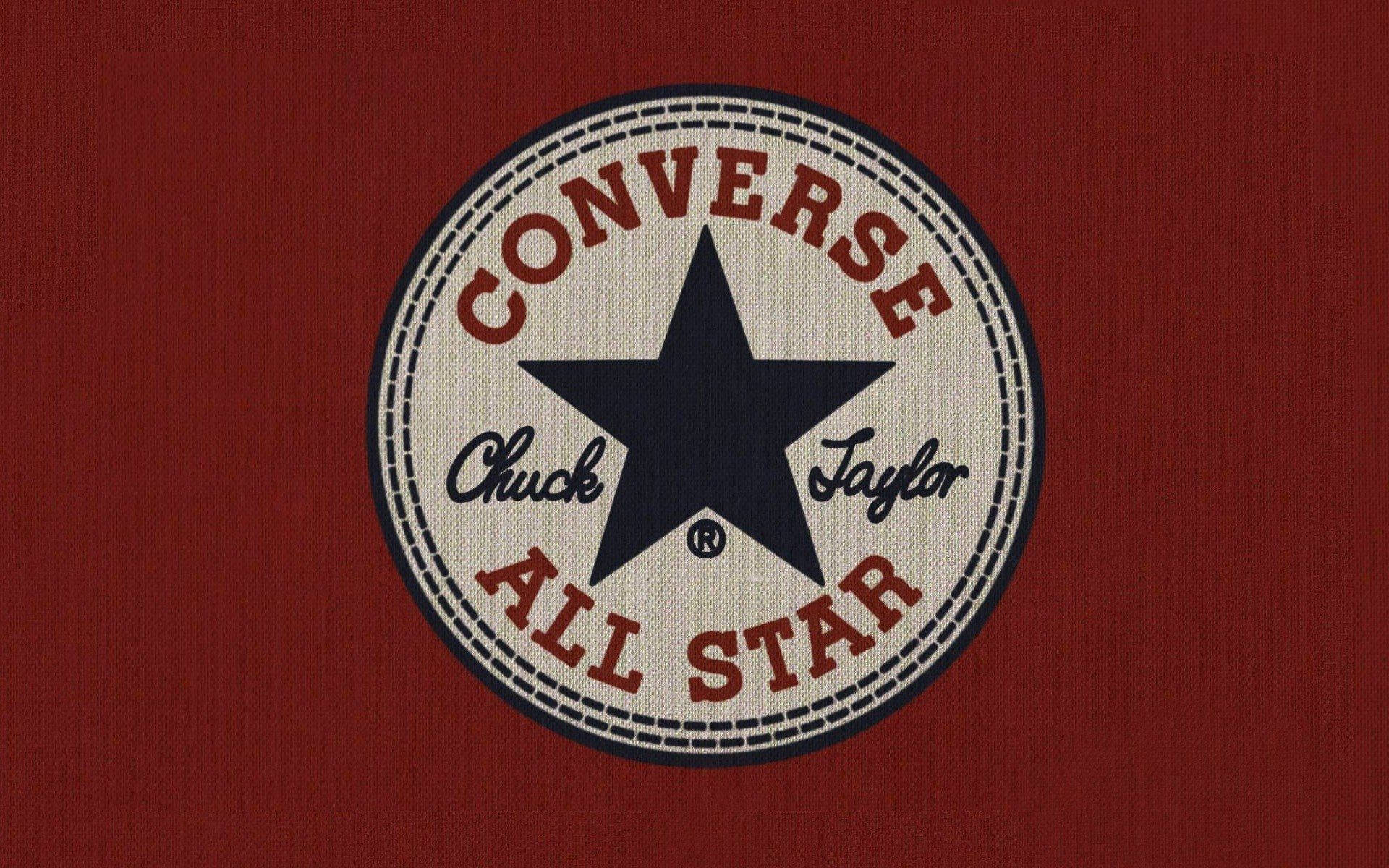 Converse Logo 桌布 壁紙 — 經典 Converse All Star 標誌貼片，海軍藍星星和紅色文字，背景為有紋理的深紅色布料。